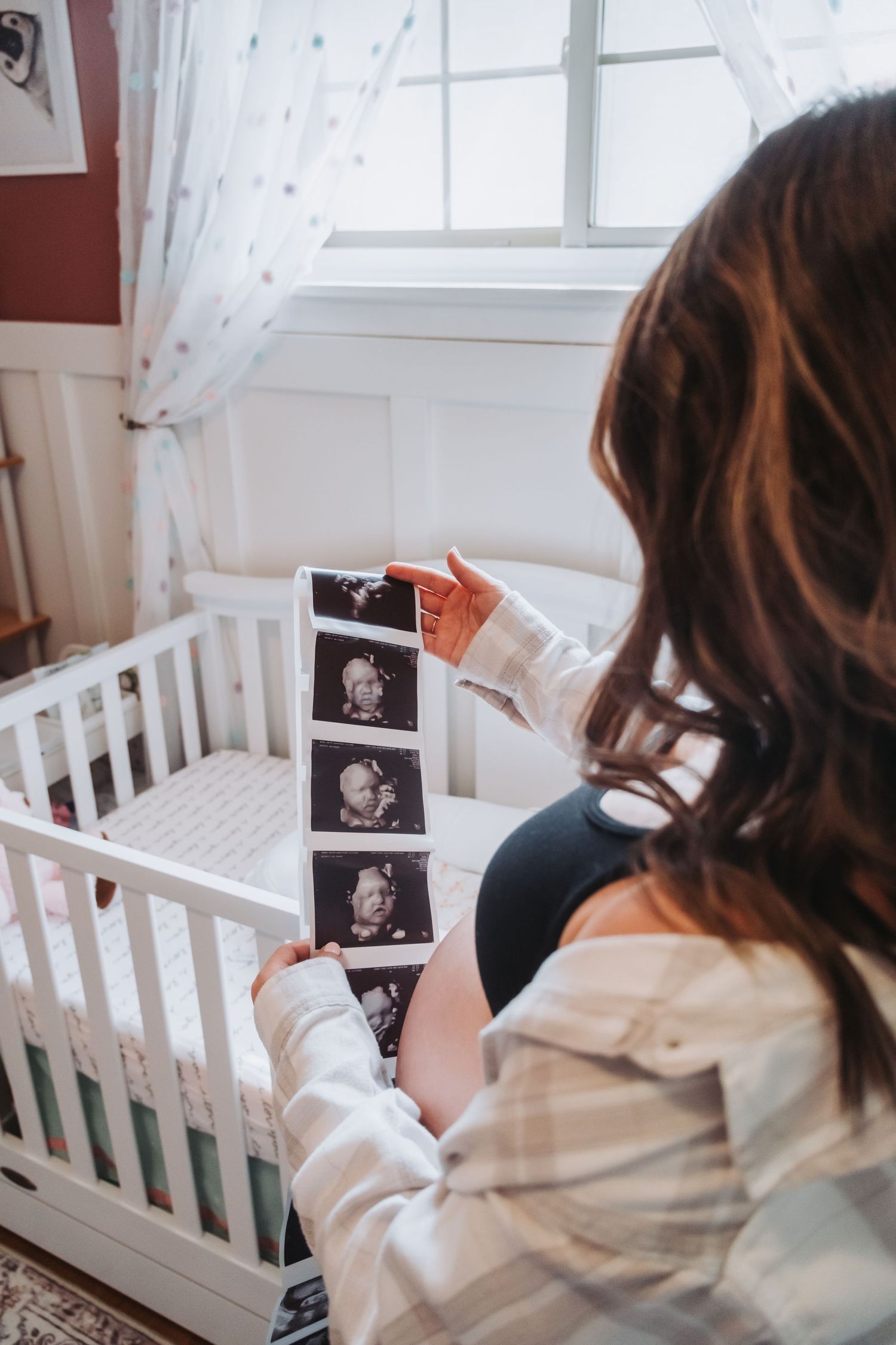 Person looking at ultrasound photos in white nursery room.