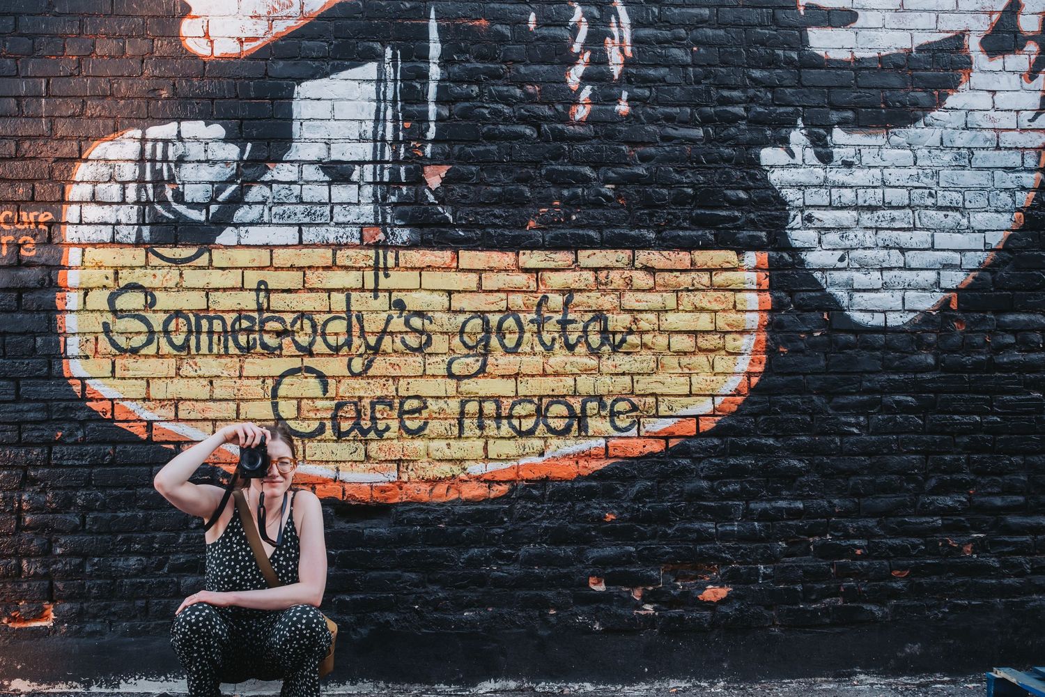 Urban brick wall mural with text and artistic designs in dark tones.