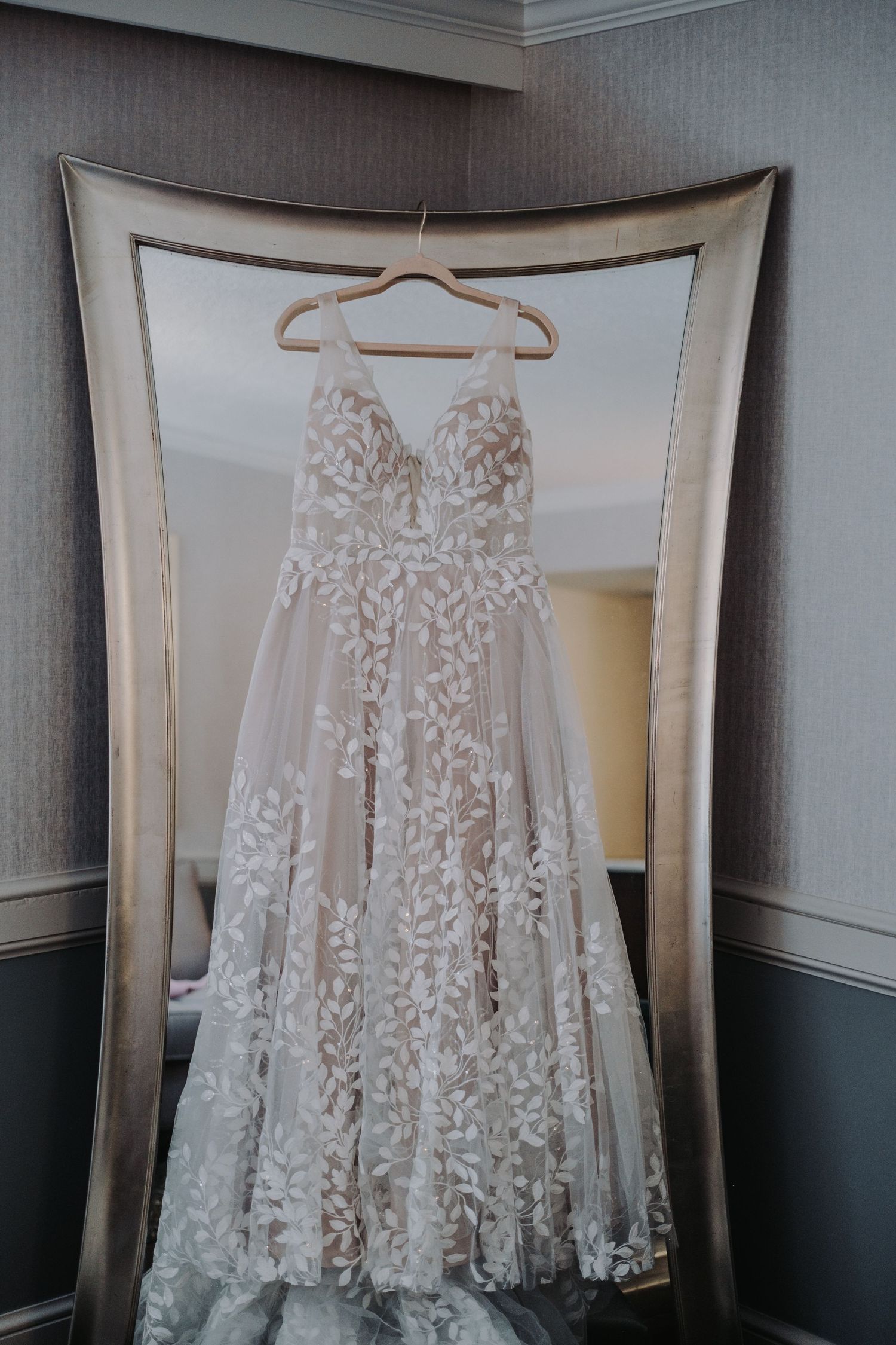Delicate white lace wedding dress with floral details hanging on display.