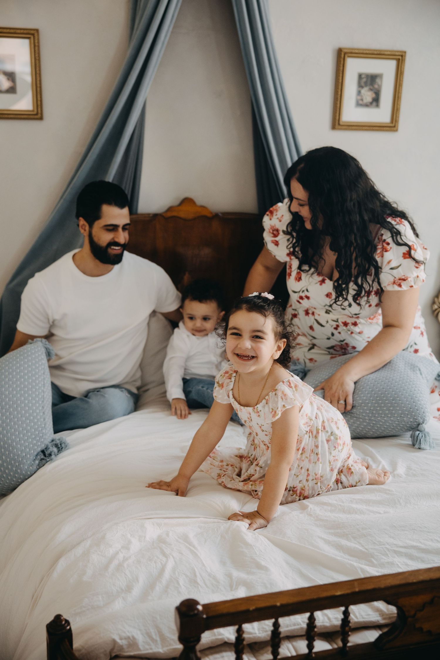 Happy family with two young children playing on a bed with blue canopy in a cozy bedroom.