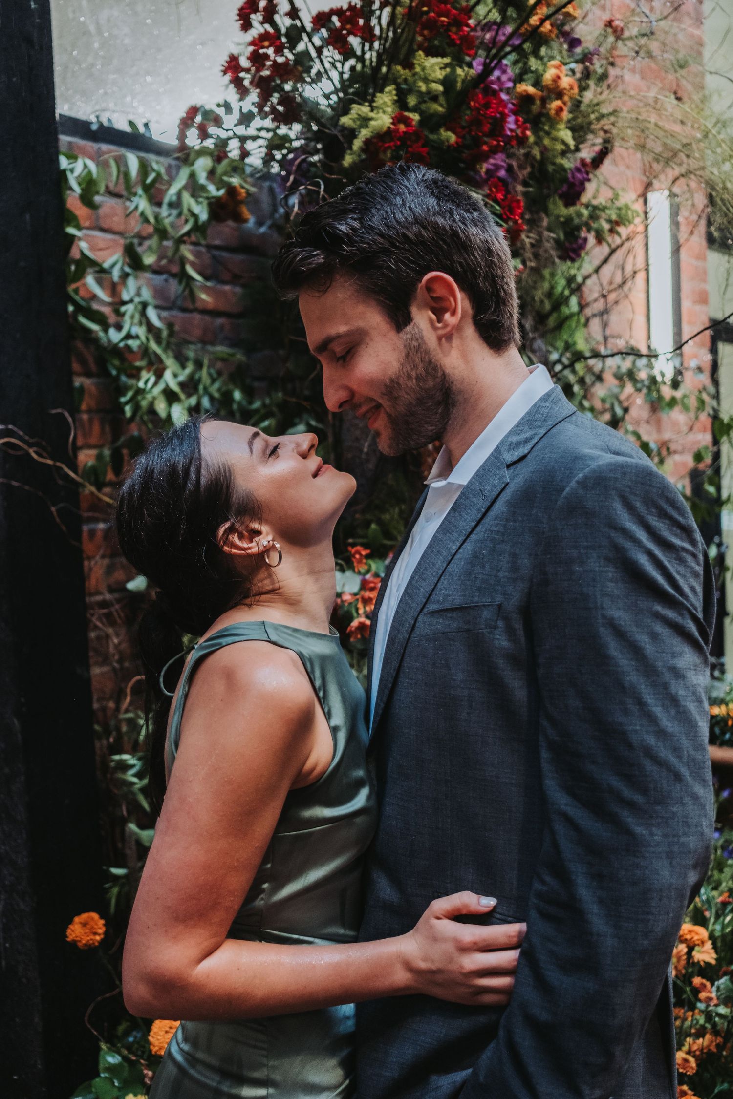 Couple in elegant attire sharing a romantic moment in front of a colorful floral backdrop.