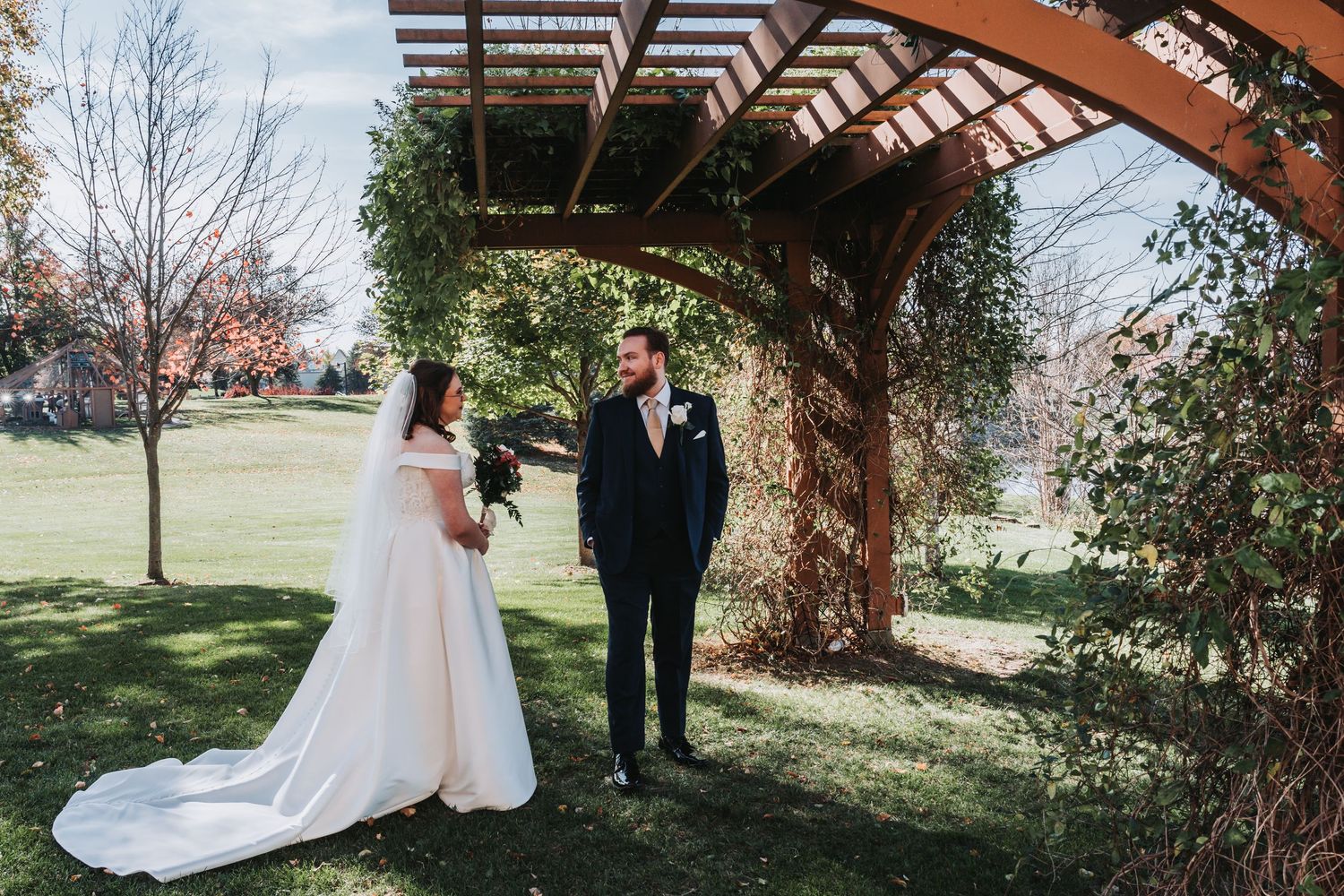Outdoor wedding photos being taken under a wooden pergola in a garden setting.