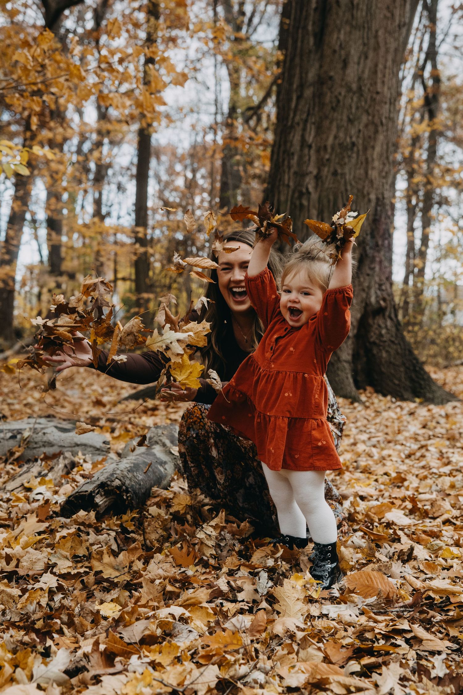 Joyful autumn scene with people playing in fallen golden leaves in a wooded forest setting.