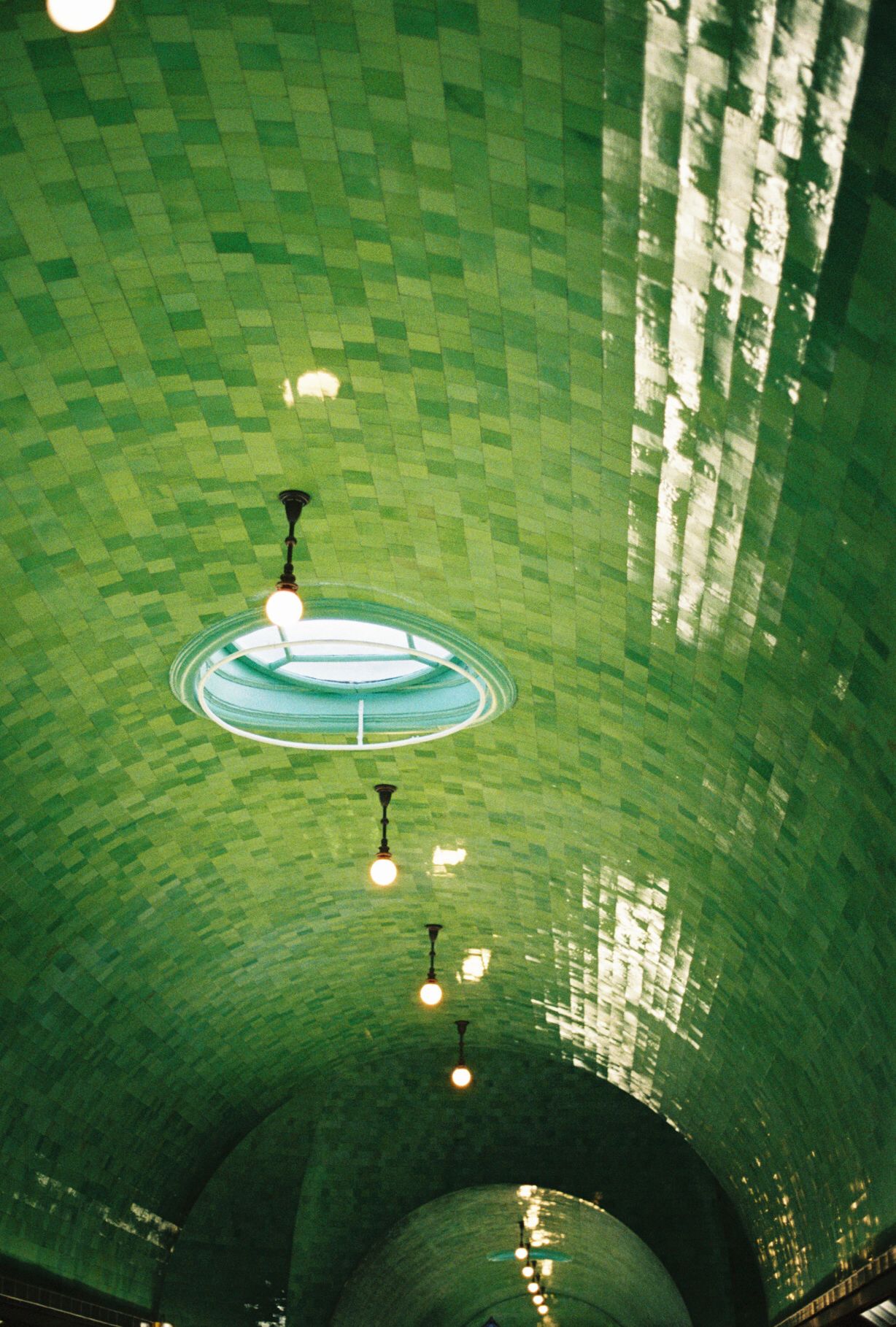 Green tiled tunnel ceiling with vintage light fixtures creates an atmospheric underground passage.