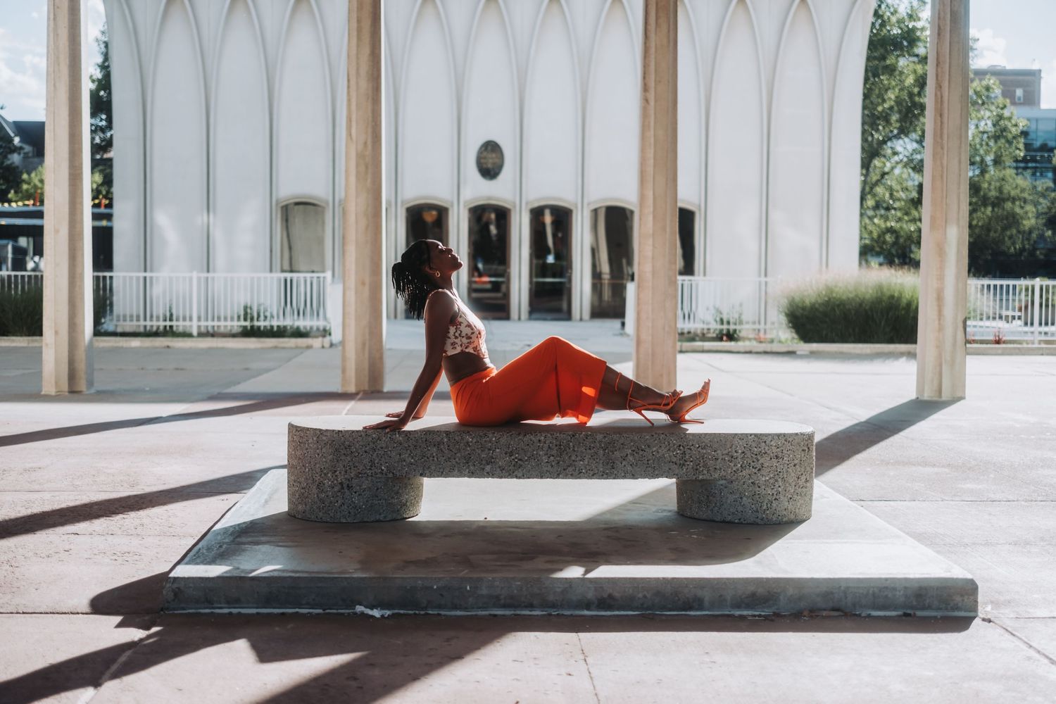 Woman in red pants posing on stone steps outside a white building with arched columns.