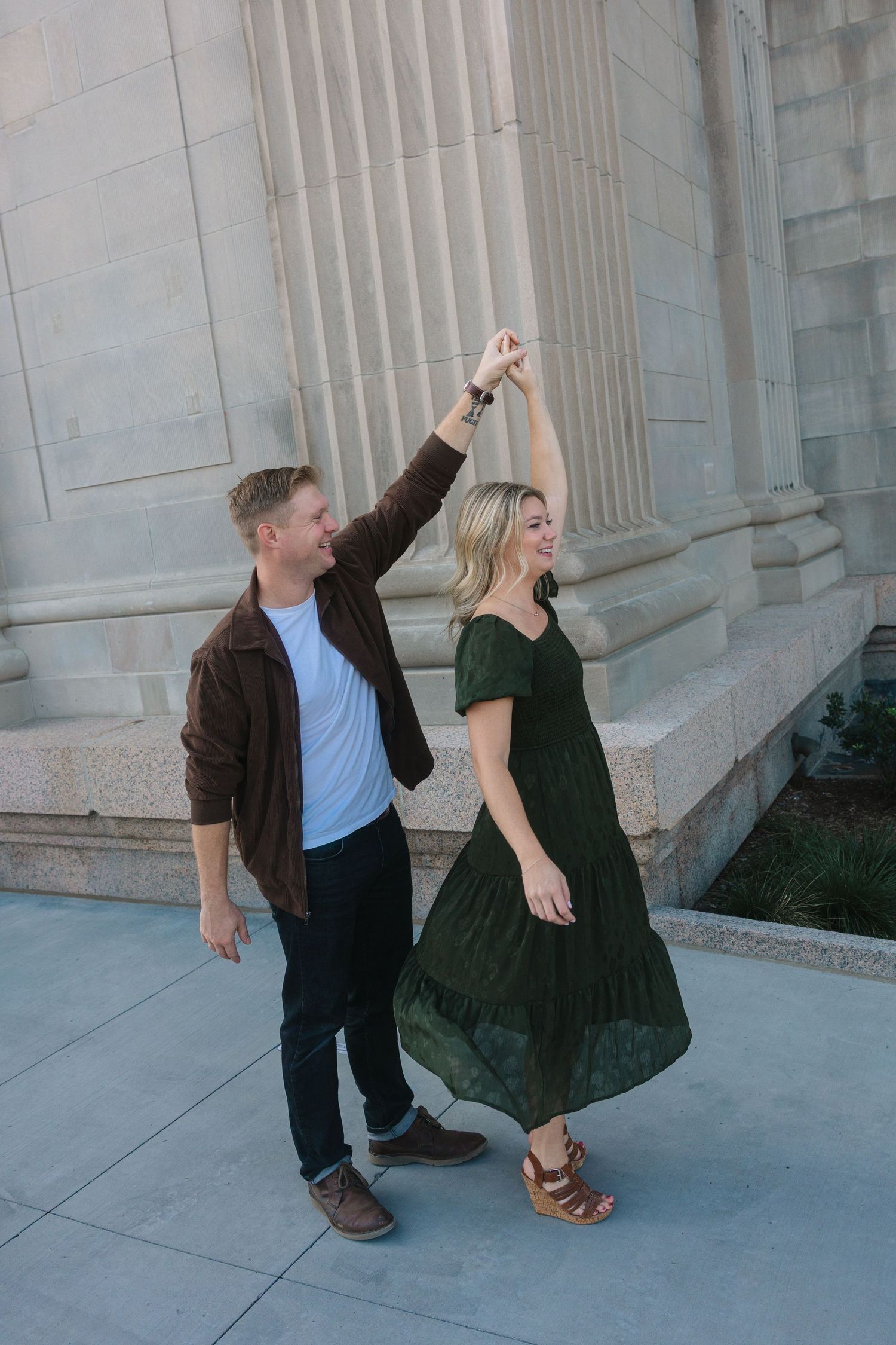 Playful couple strikes dynamic poses against classical stone building columns.
