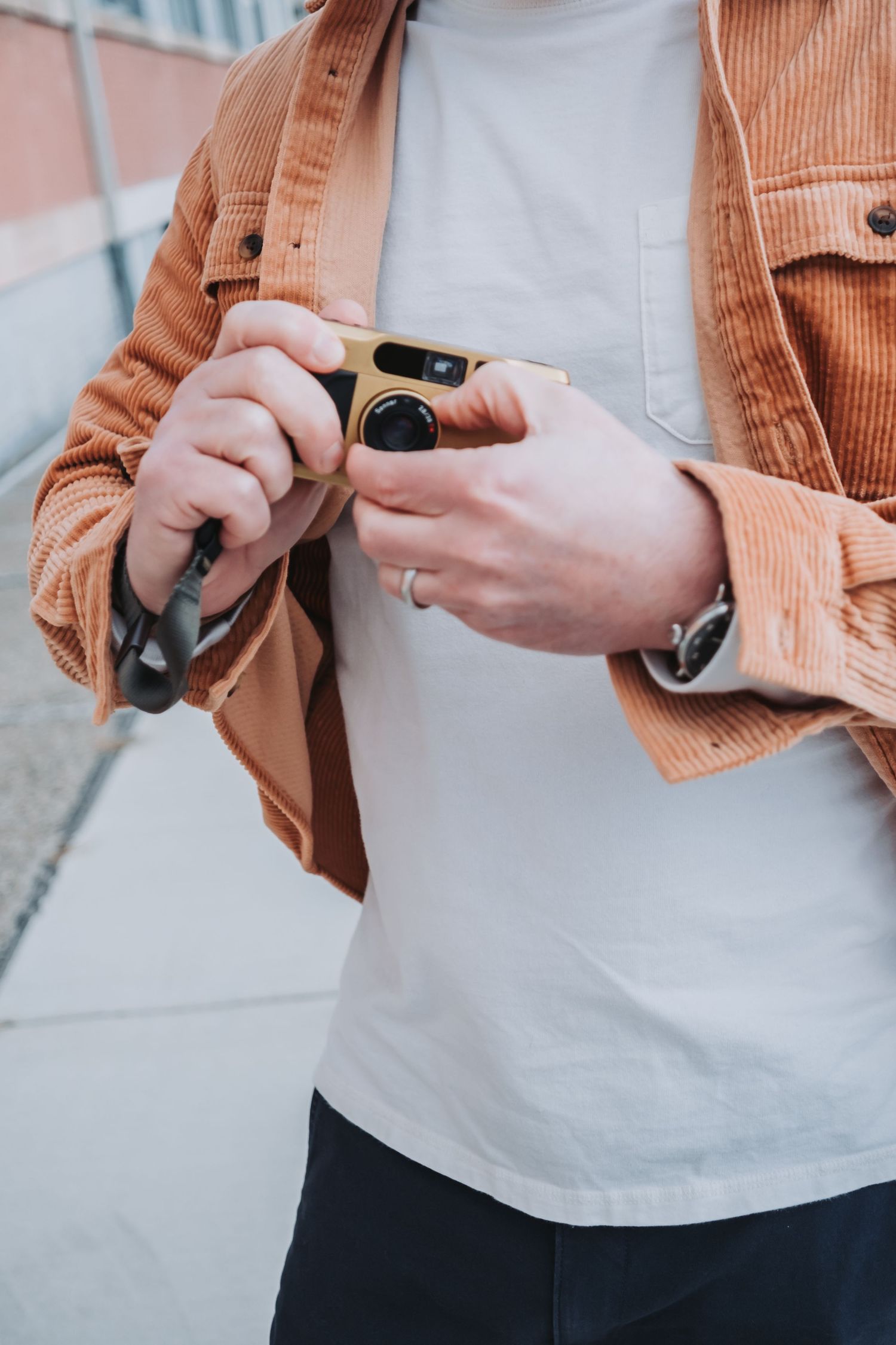 Person wearing coral jacket holding camera, close-up of hands and torso.
