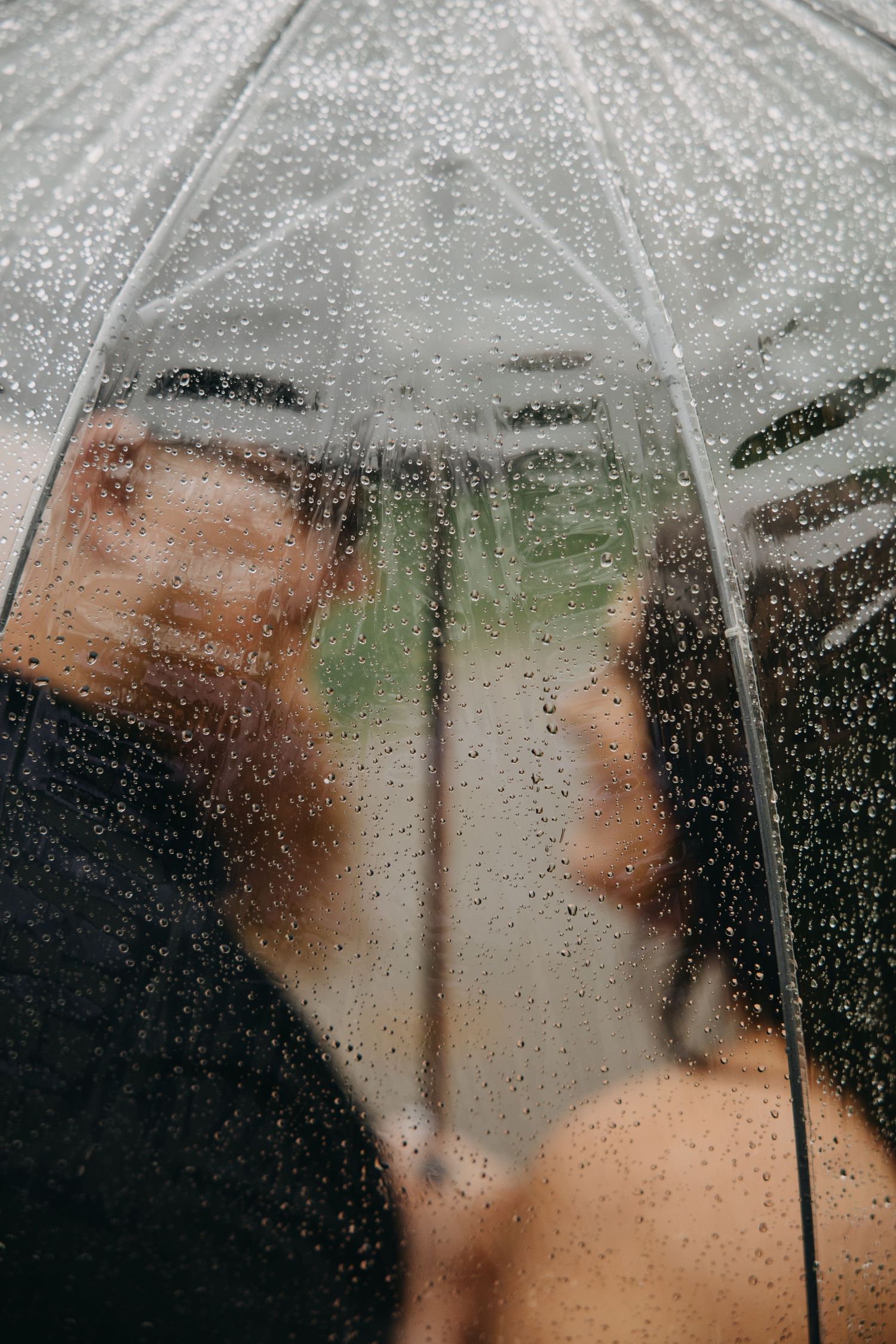 Couple sharing a romantic moment under a clear umbrella covered in raindrops on a rainy day.