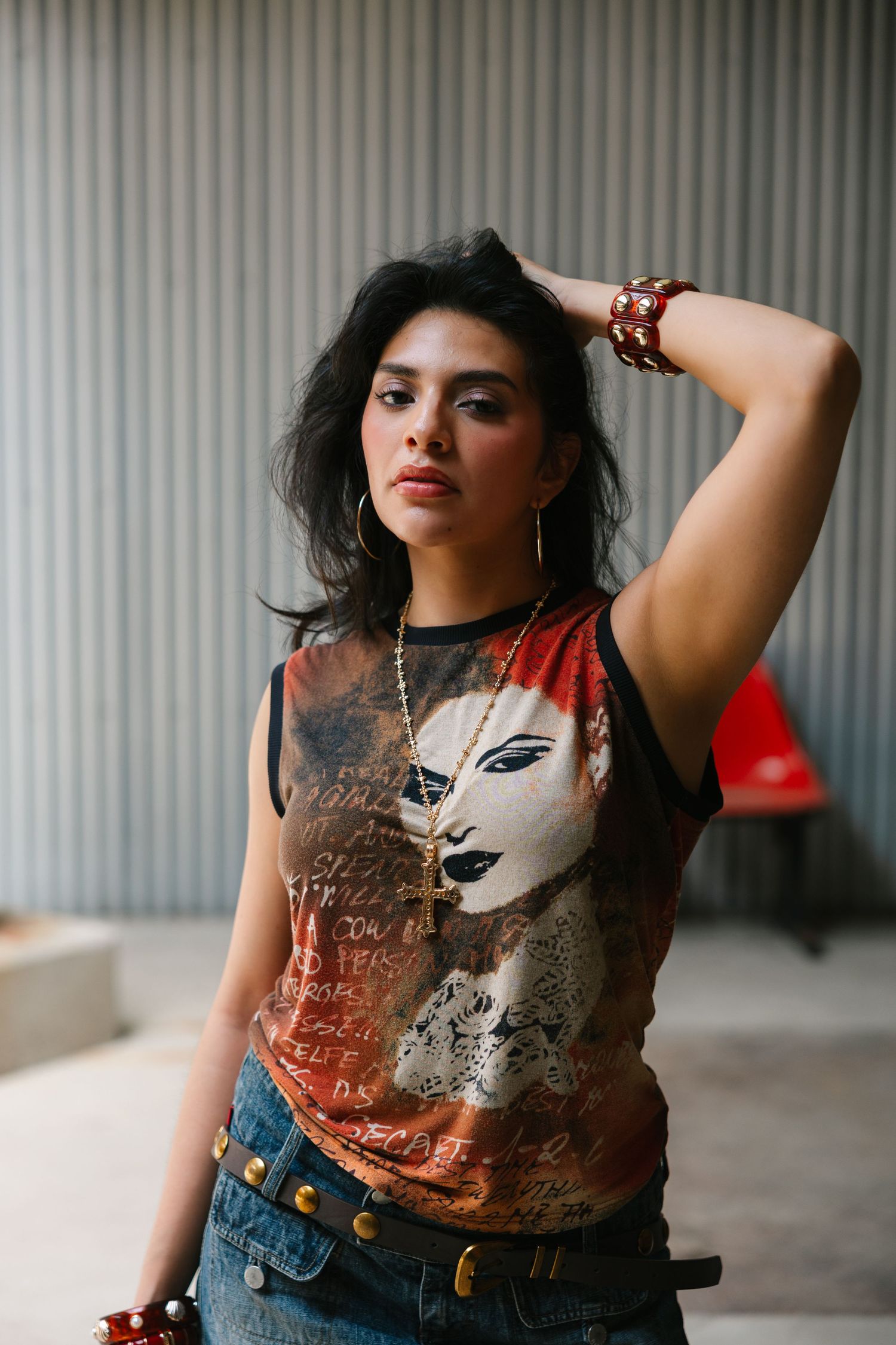 Young woman in graphic tee, denim jeans, and red accessories poses confidently indoors.