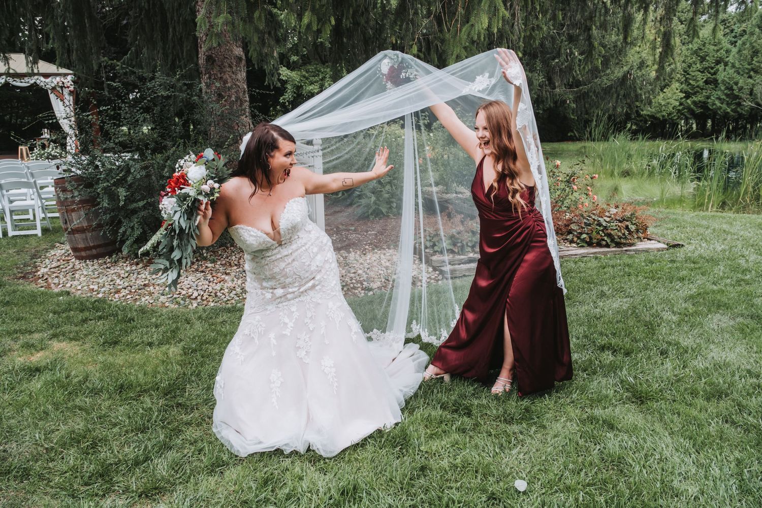 Wedding couple playing with veil in garden setting.
