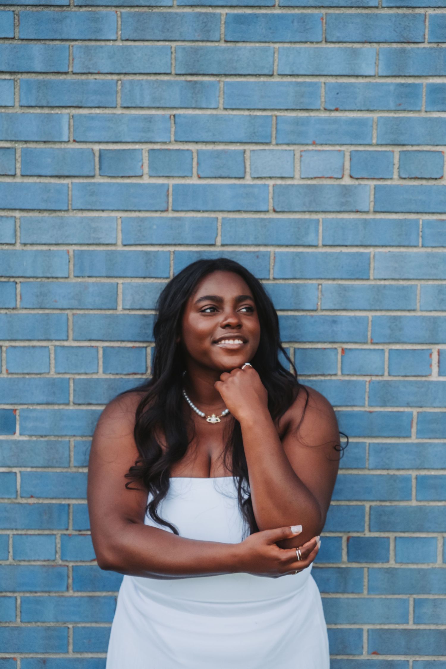 Portrait against blue brick wall showcasing elegant white dress and natural pose.