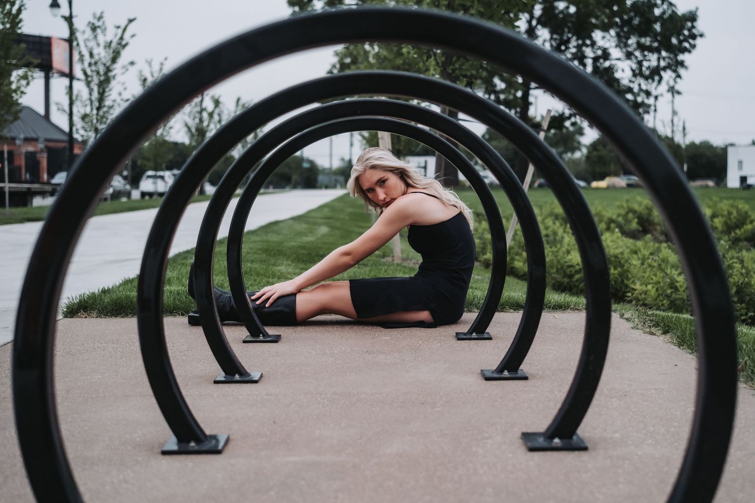 Woman in black athletic wear stretching inside circular metal bike rack sculpture in an outdoor park setting.