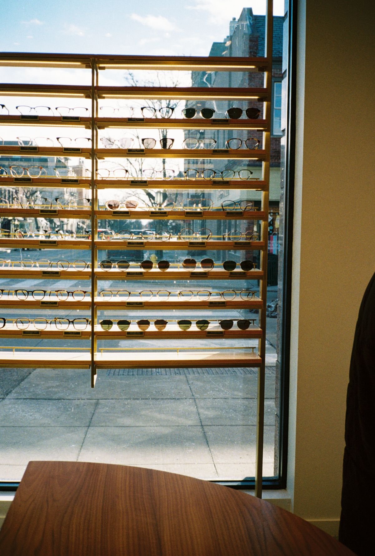 Retail display showing rows of eyeglasses on wooden shelves near a window.