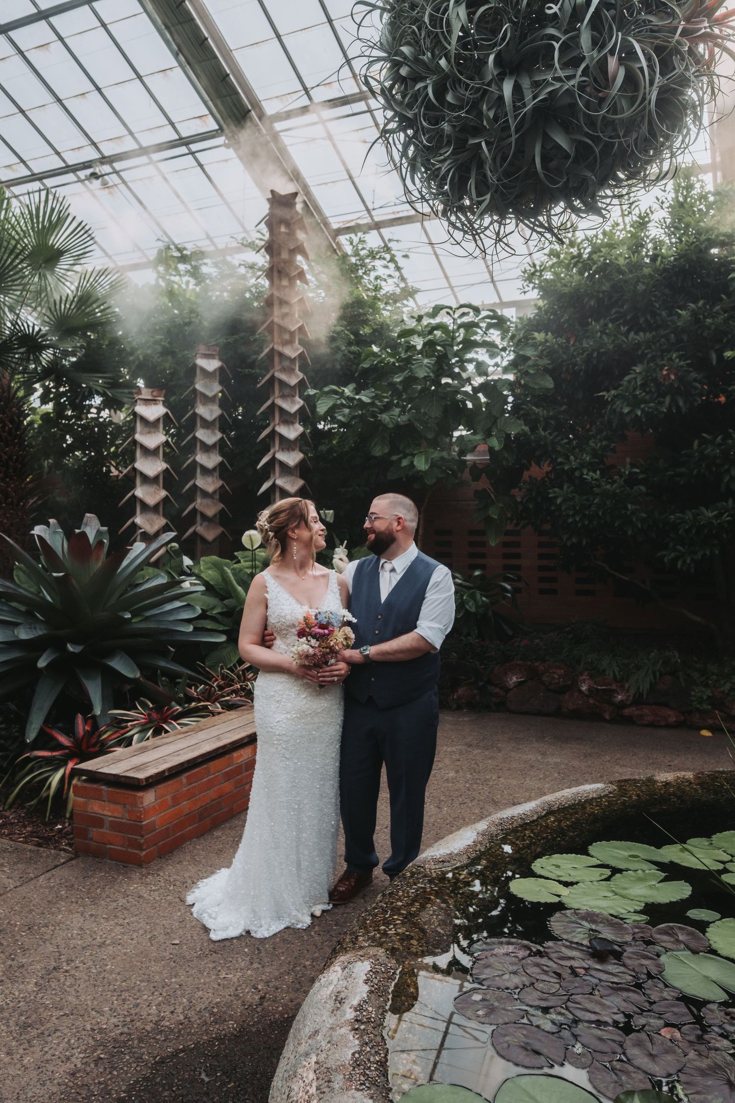 An intimate wedding ceremony taking place in a botanical garden greenhouse with lush greenery.