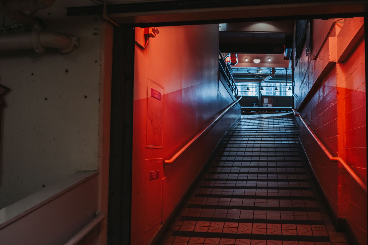 Dark stairway with red lighting leading down to a corridor in an urban building interior.