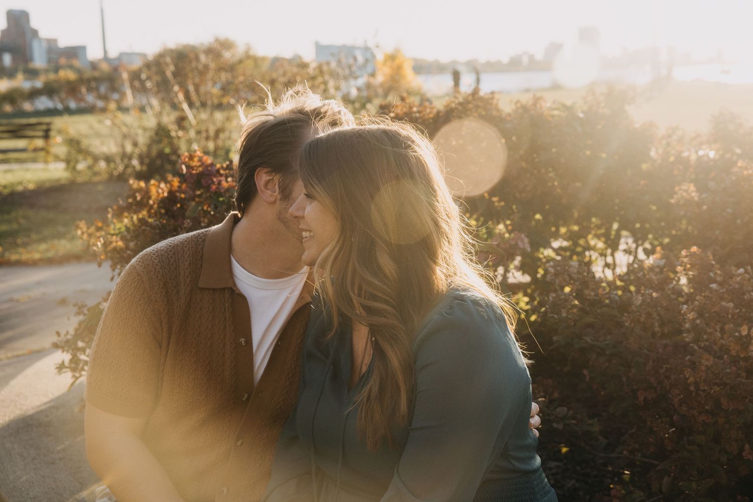 Couple sharing a romantic moment outdoors in golden sunset light, surrounded by autumn foliage in a park setting.