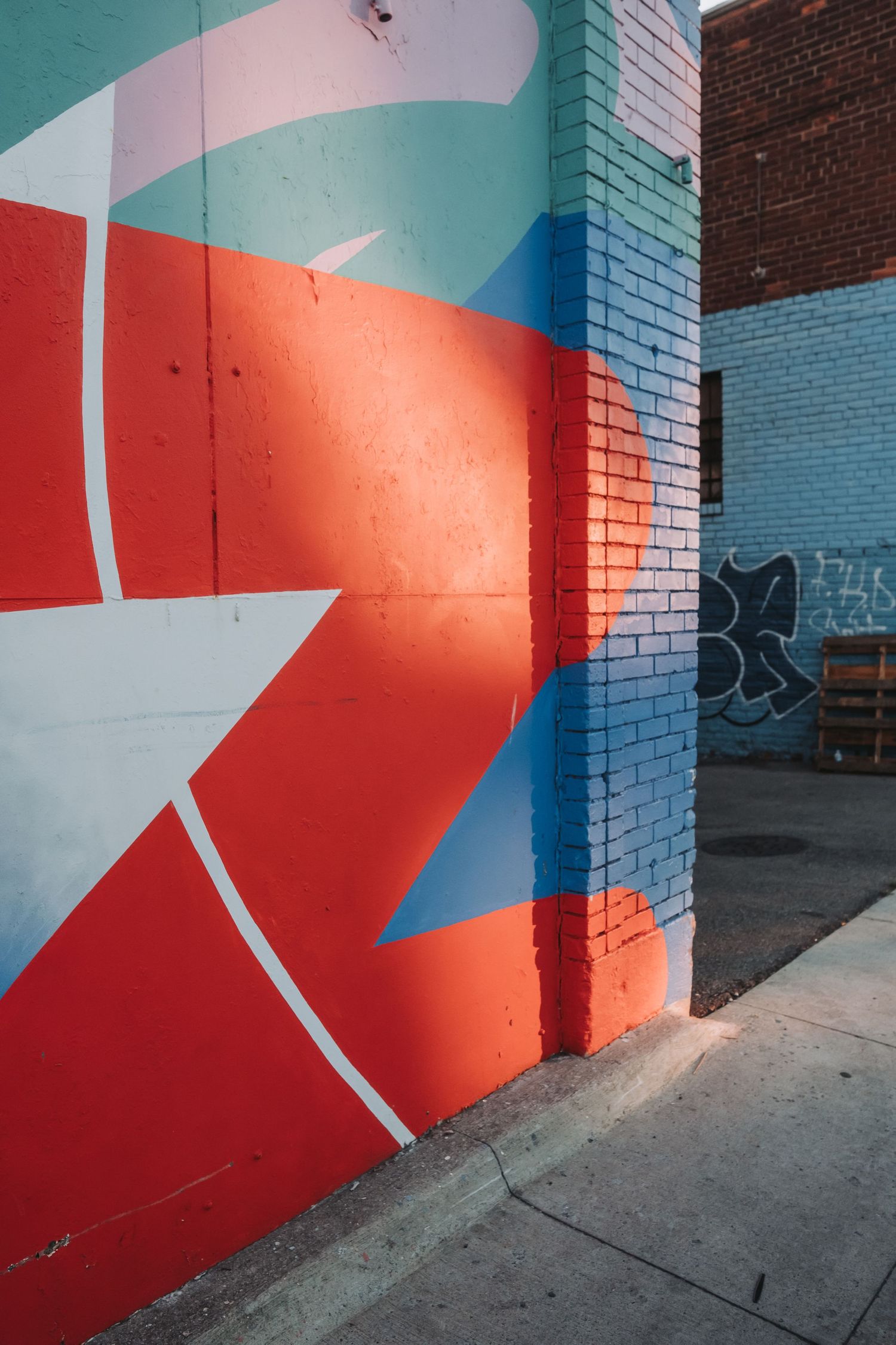 Abstract geometric mural with red, blue and white shapes painted on brick wall.