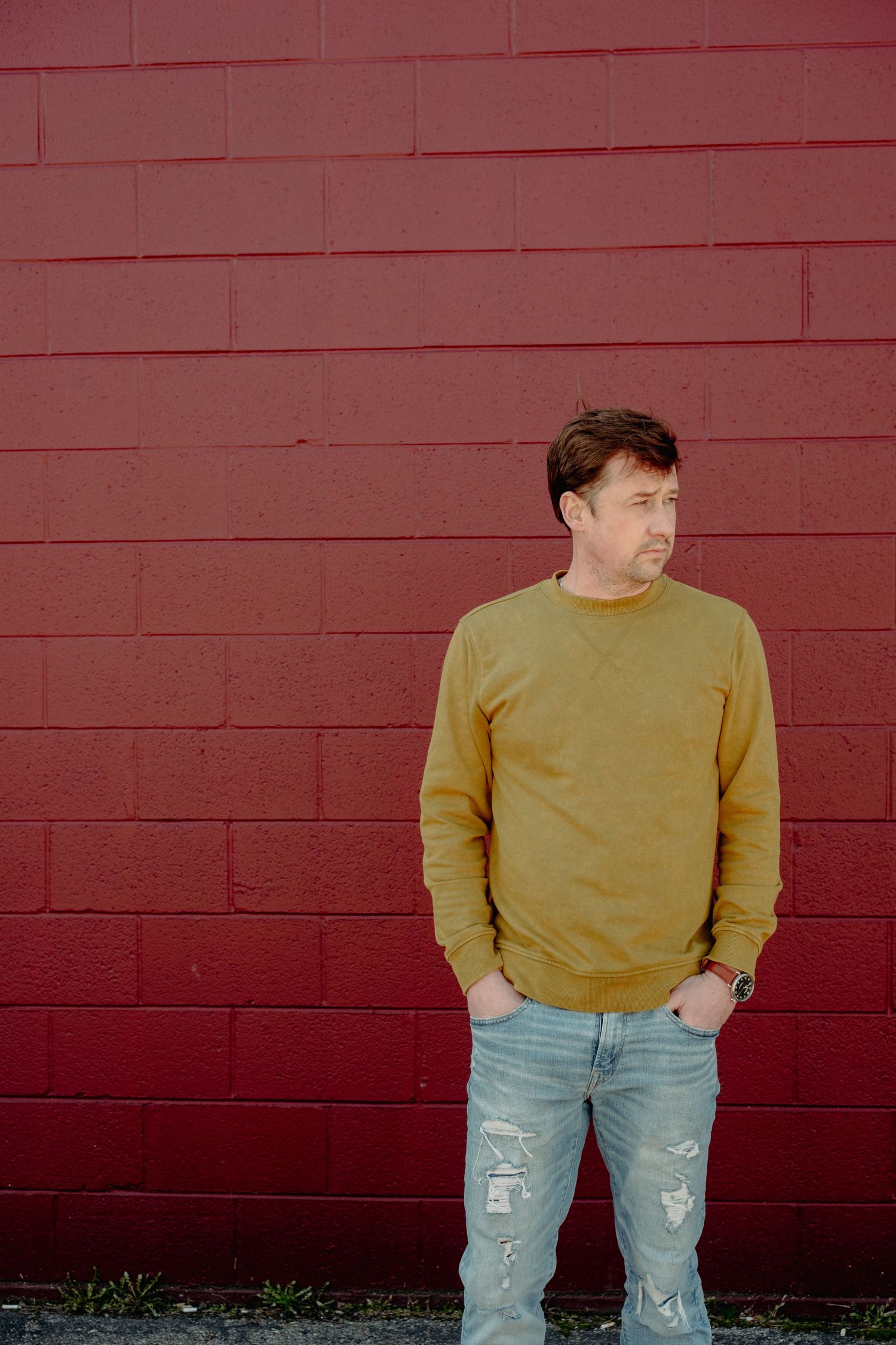 Person wearing yellow sweater and distressed jeans poses against red wall in segmented photo series.