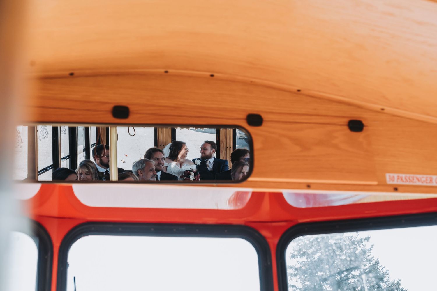 Passengers visible through rearview mirror of a vintage orange school bus interior.