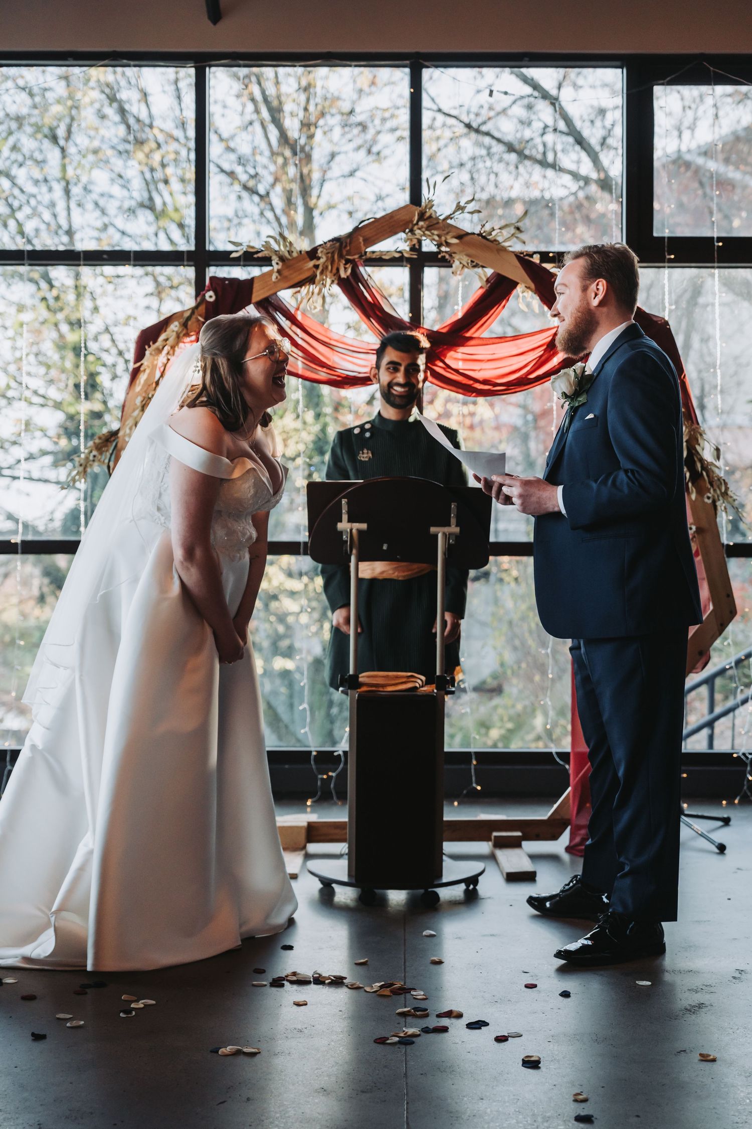 Bride and groom exchange vows under floral arch with officiant at indoor wedding ceremony.