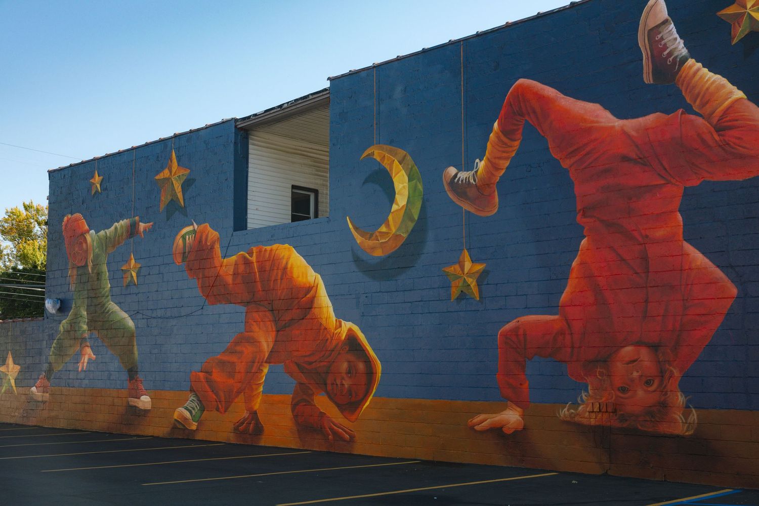 Colorful mural depicting orange dinosaurs with stars and moons against a deep blue background on a building wall.