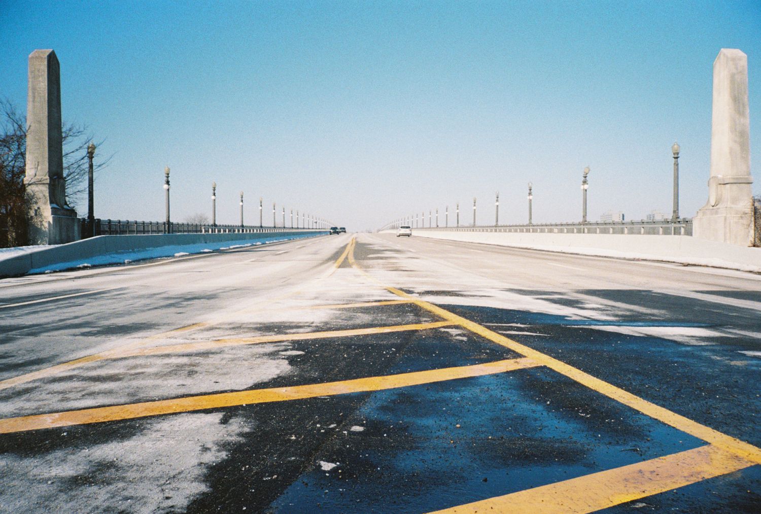 Empty parking lot with yellow lines covered in snow and utility poles in the distance.