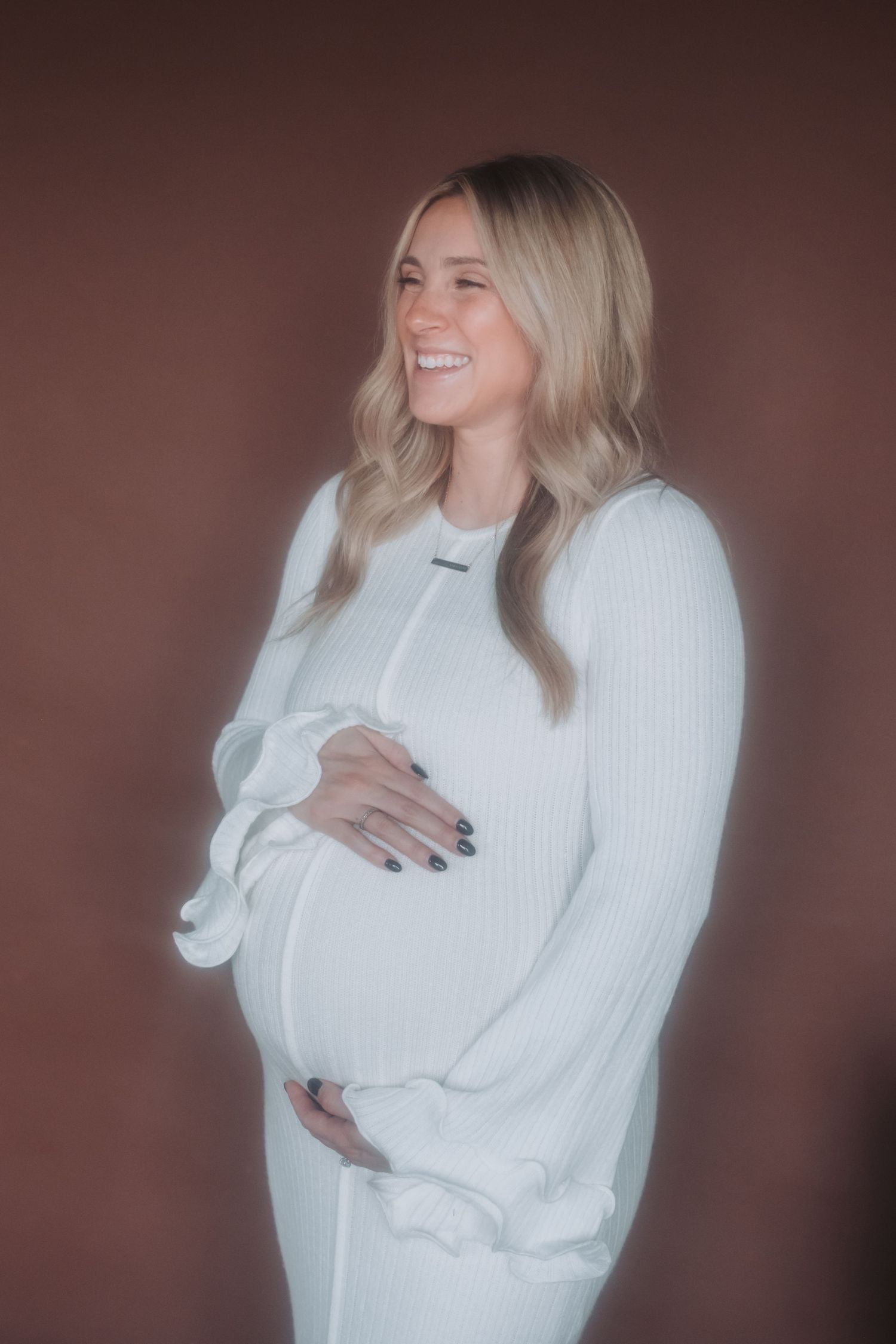 Woman in white sweater poses against brown background.