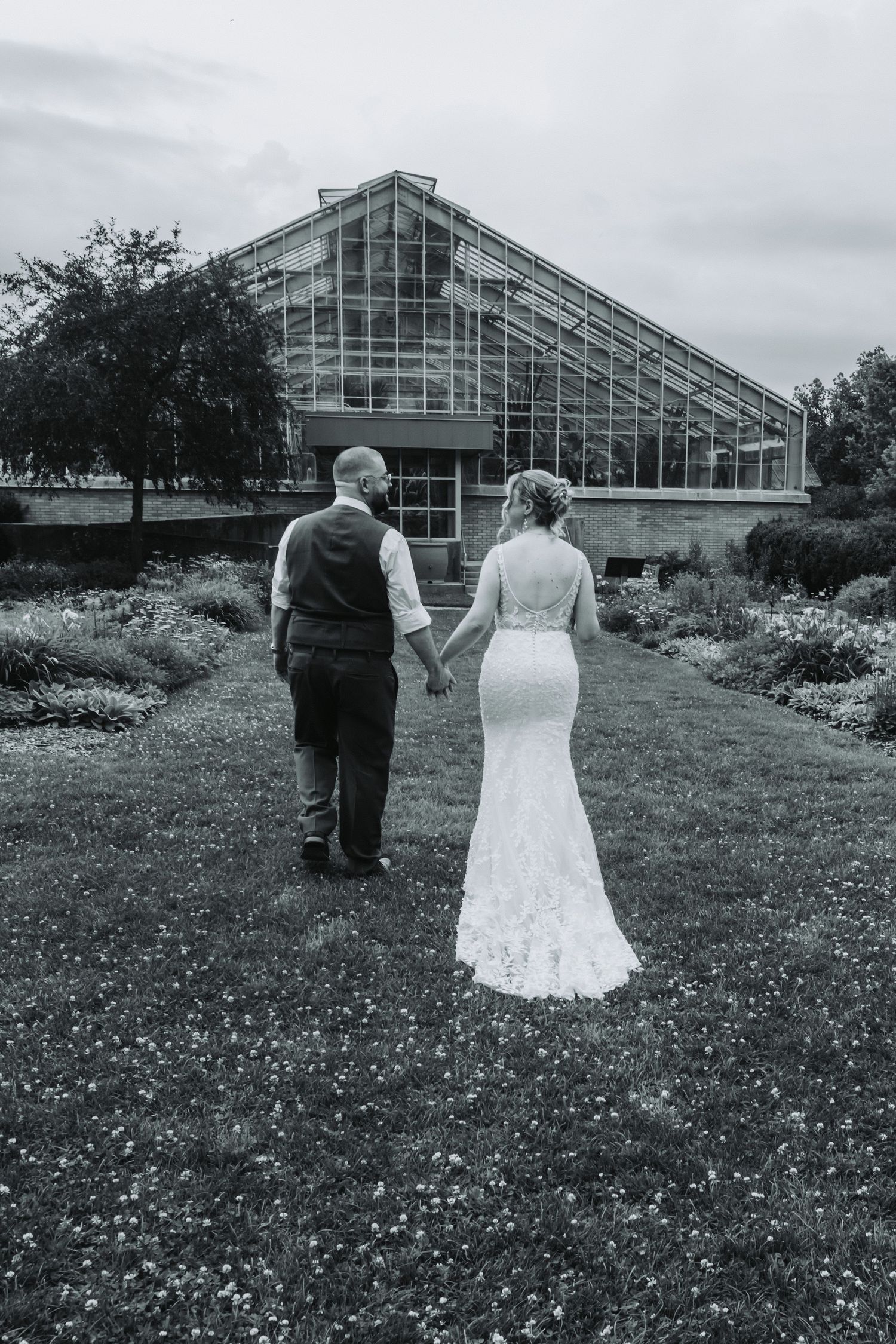 Black and white photo of a couple walking towards a modern greenhouse structure.
