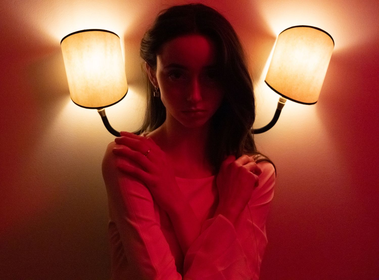 A woman poses between two glowing wall sconces in warm red ambient lighting.