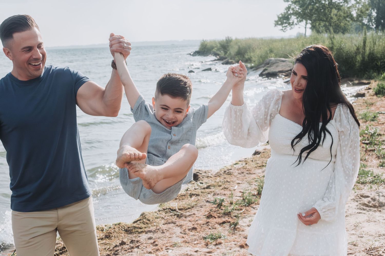 Family of three enjoying a beach day, parents swinging their smiling son between them on a sandy shore.