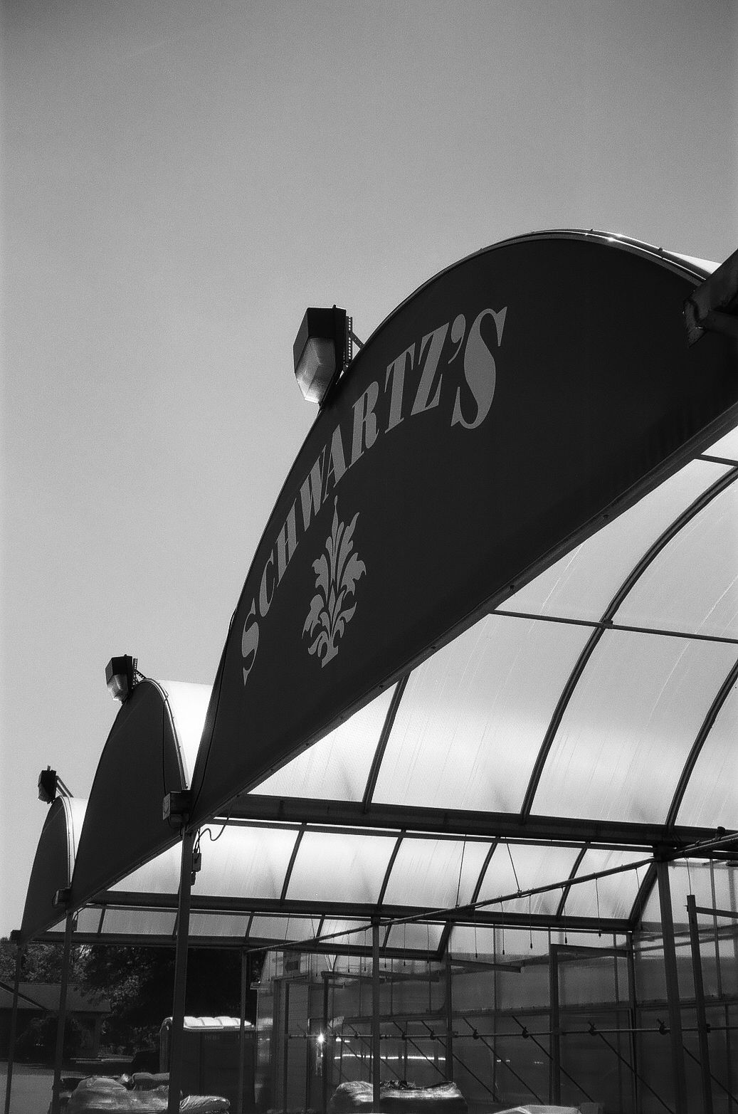 Black and white photo of Schwartz's restaurant sign on a curved greenhouse-style canopy structure.