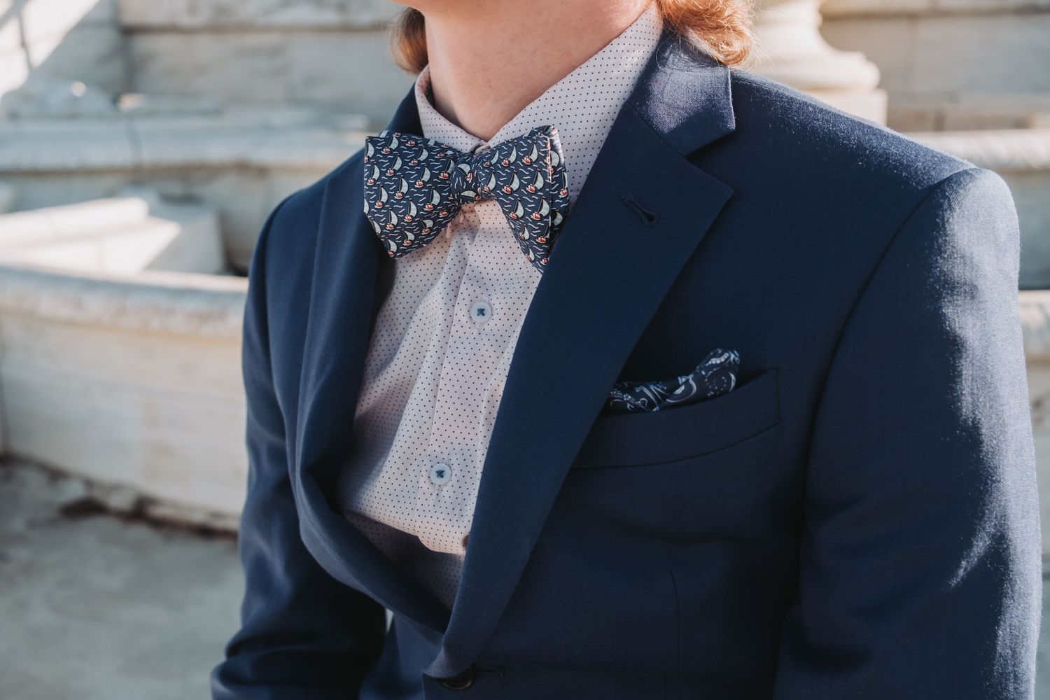 Man in navy blue suit with patterned bow tie and matching pocket square, dressed in smart formal attire.