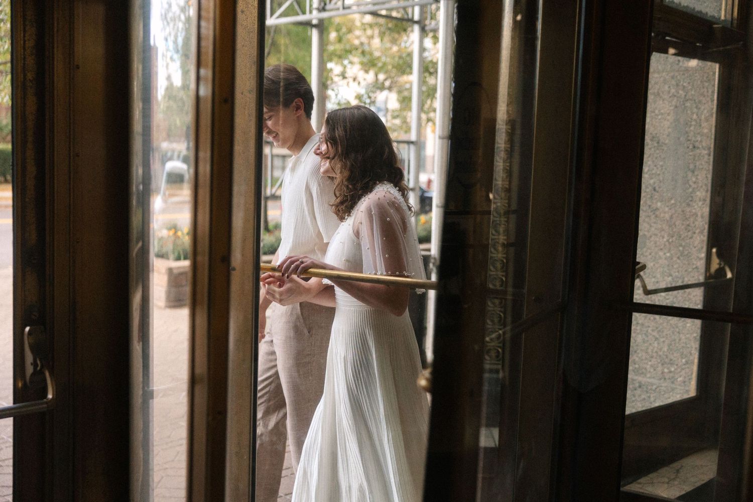 A bride in a flowing white gown and groom stand together in an elegant doorway during their wedding day.