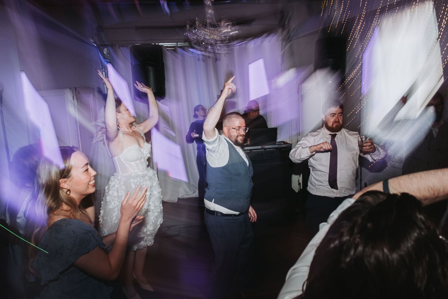 Energetic dancing and celebration on a dimly lit dance floor at a reception party.