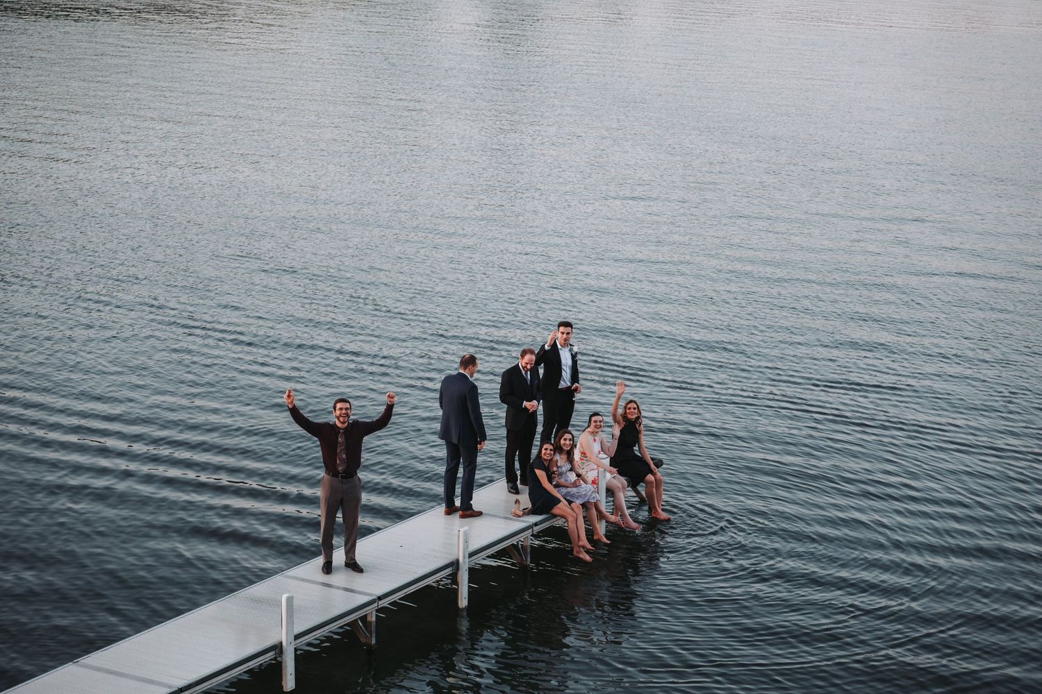Wedding guests jump off a dock into a lake creating splashes in the water.