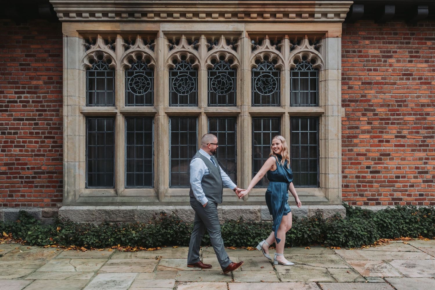 Couple dancing playfully in front of historic Gothic-style building with ornate windows.
