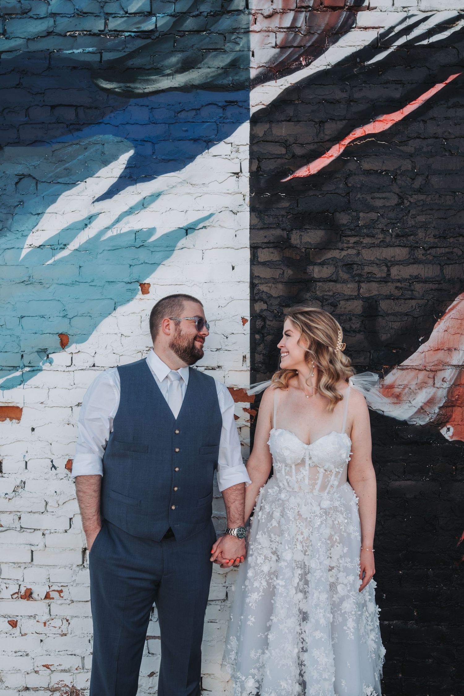 Bride and groom holding hands smiling before a colorful street mural on their wedding day.