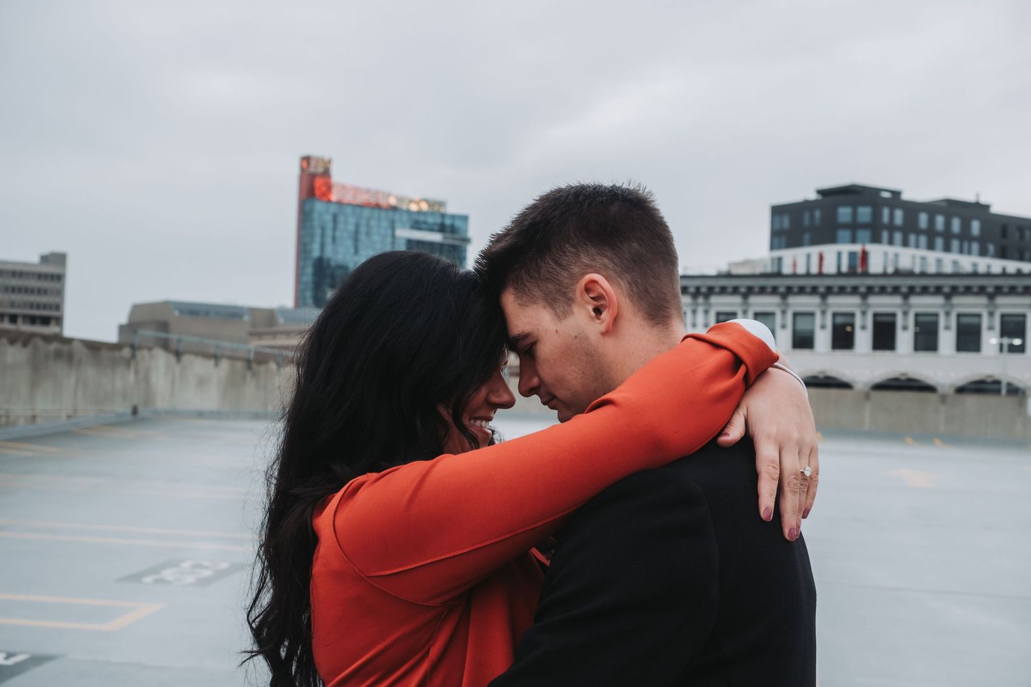 Couple sharing romantic embrace on rooftop with city skyline in background on cloudy day.