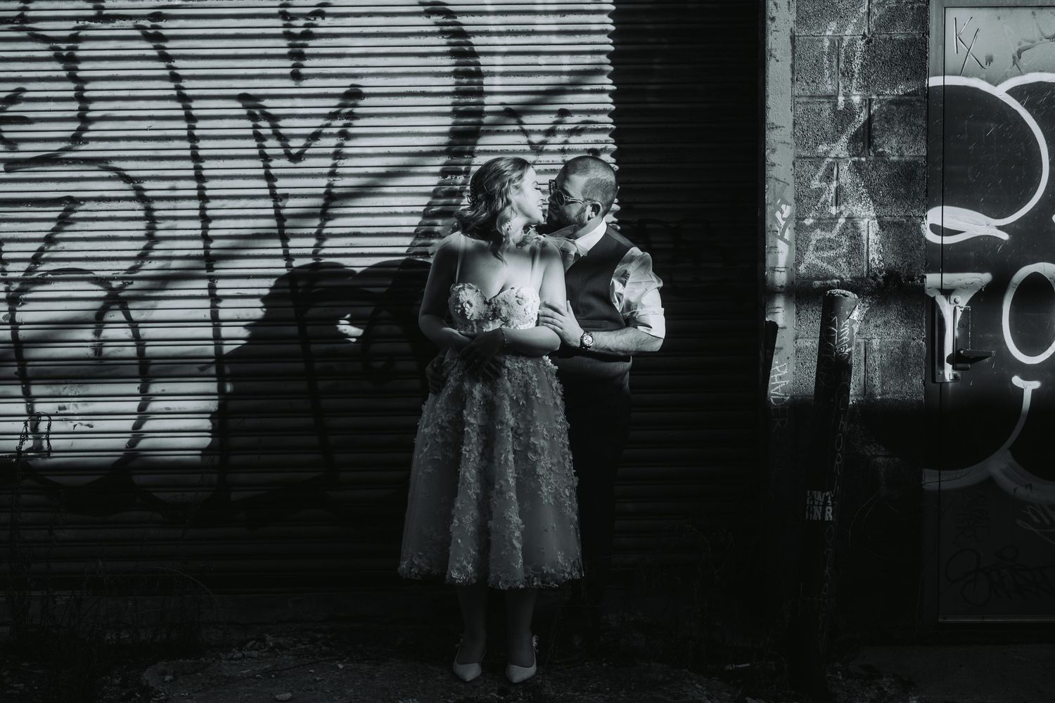 Black and white artistic portrait of couple against urban wall with graffiti.