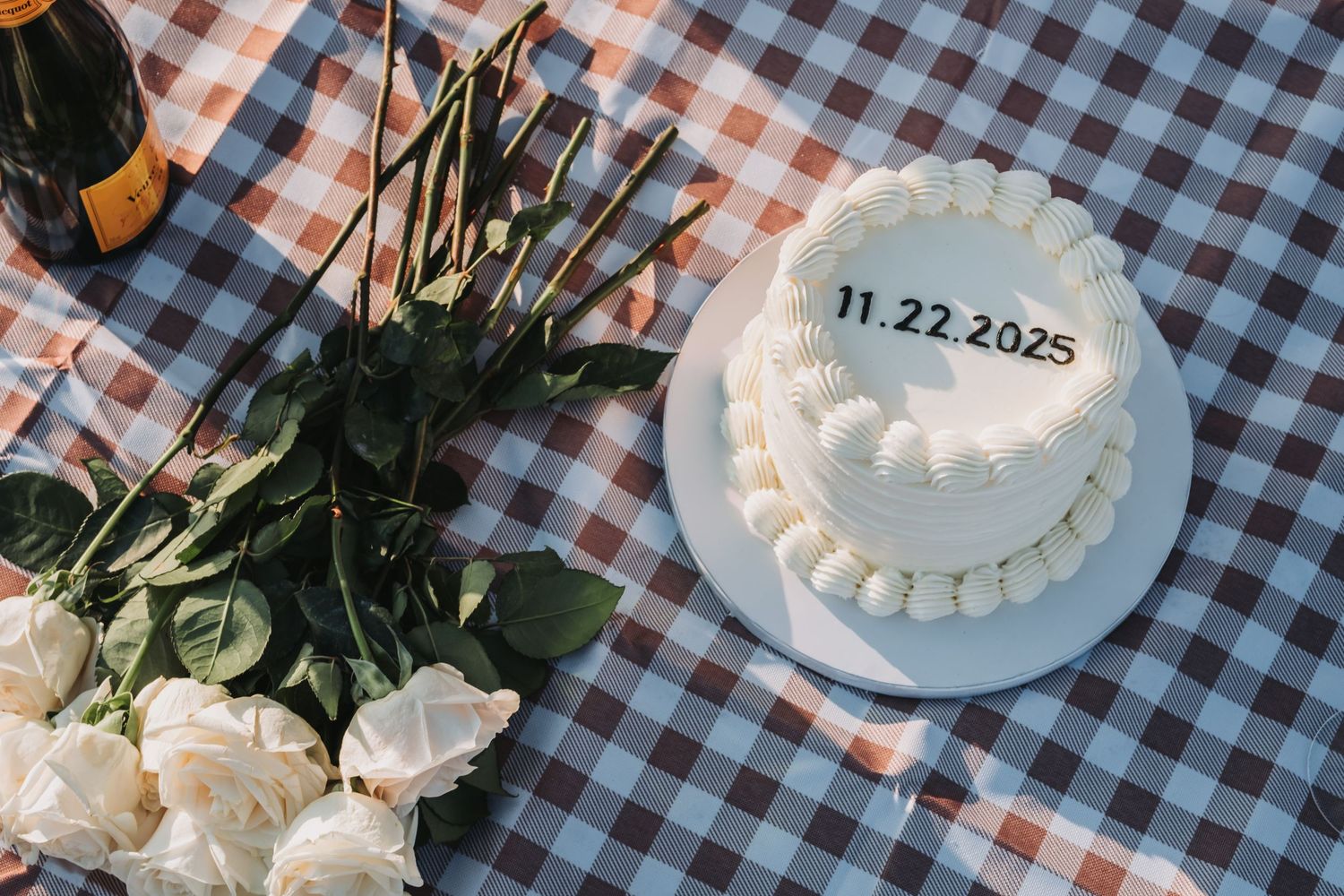 White frosted cake with floral decorations on a checkered tablecloth.