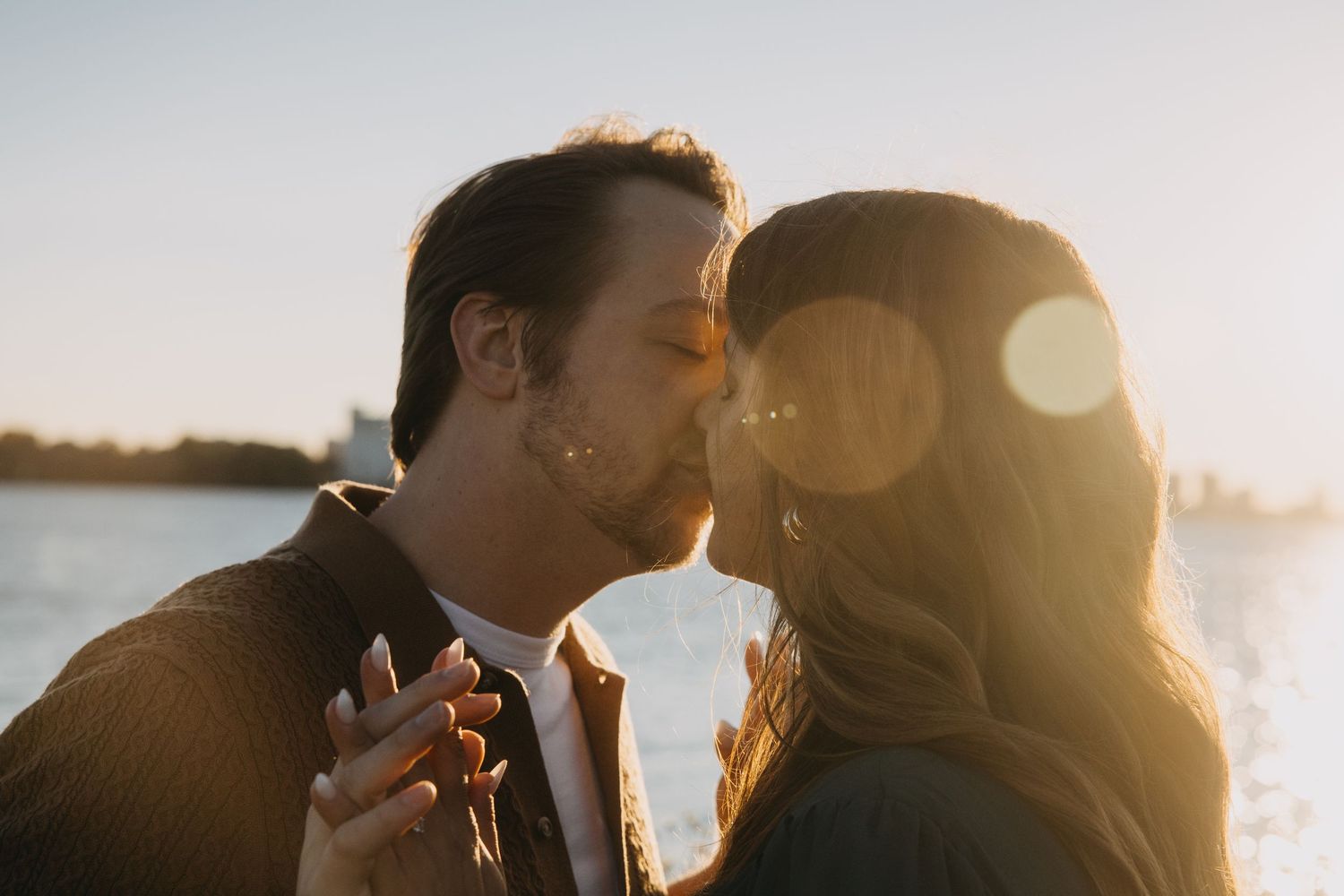 Romantic couple silhouettes embrace and kiss during golden sunset by the ocean.