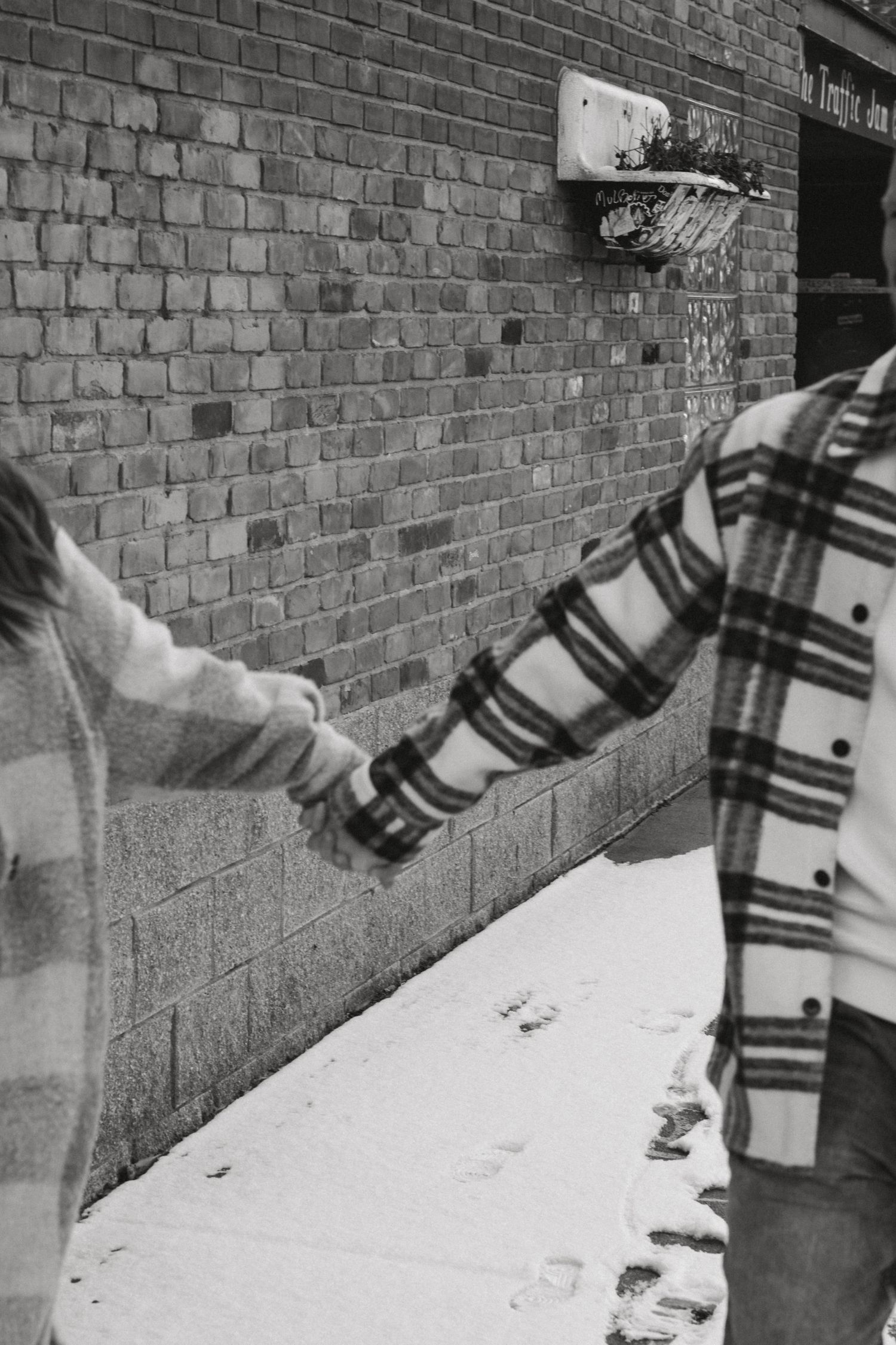 Person in plaid jacket touching a brick wall covered in snow.
