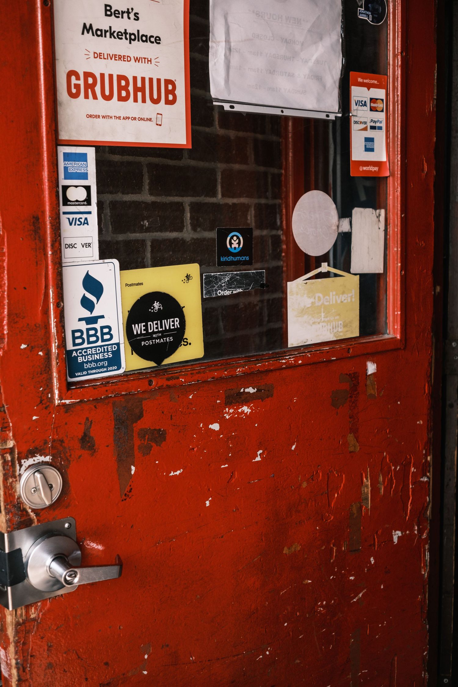 Red door with various delivery service and payment stickers at Bert's Marketplace.