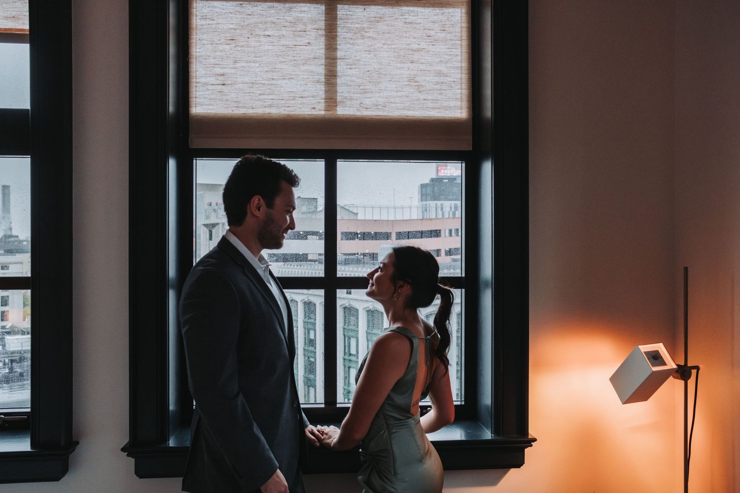 Couple sharing an intimate moment by large windows in an elegant urban venue with warm lighting.