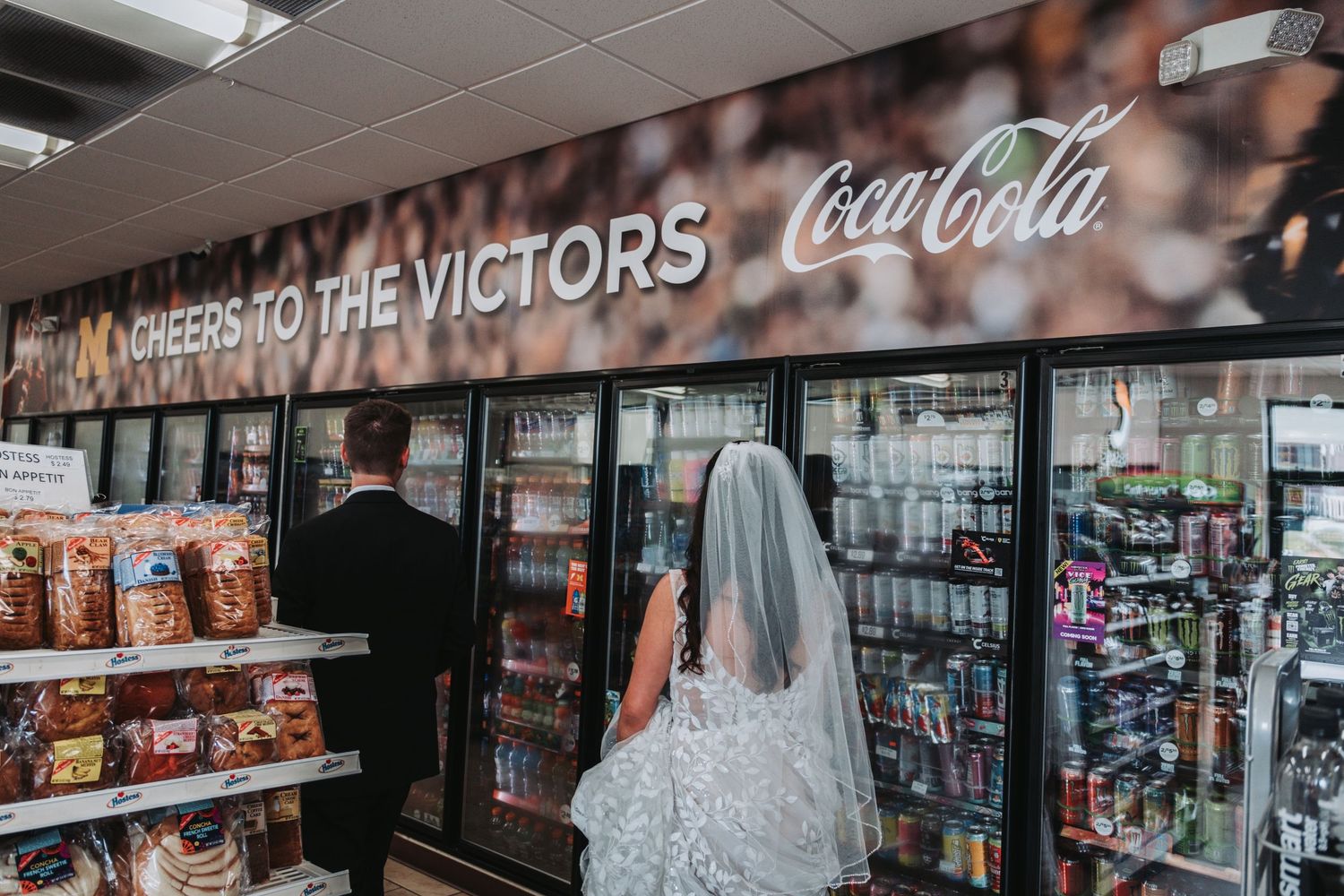 Refrigerated drink coolers filled with Coca-Cola products line the wall of a convenience store.