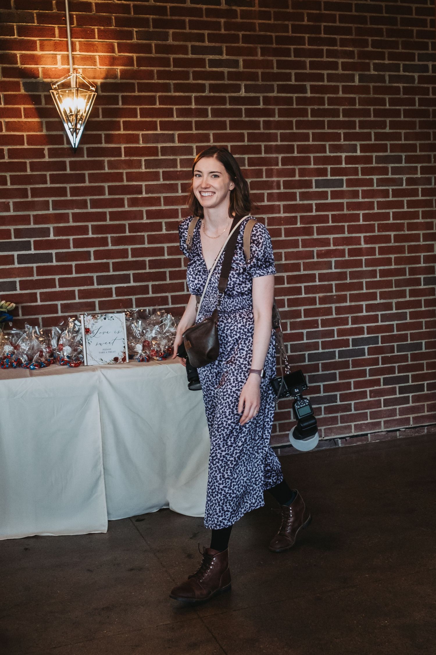 Woman in polka dot dress poses playfully against brick wall with vintage lighting.