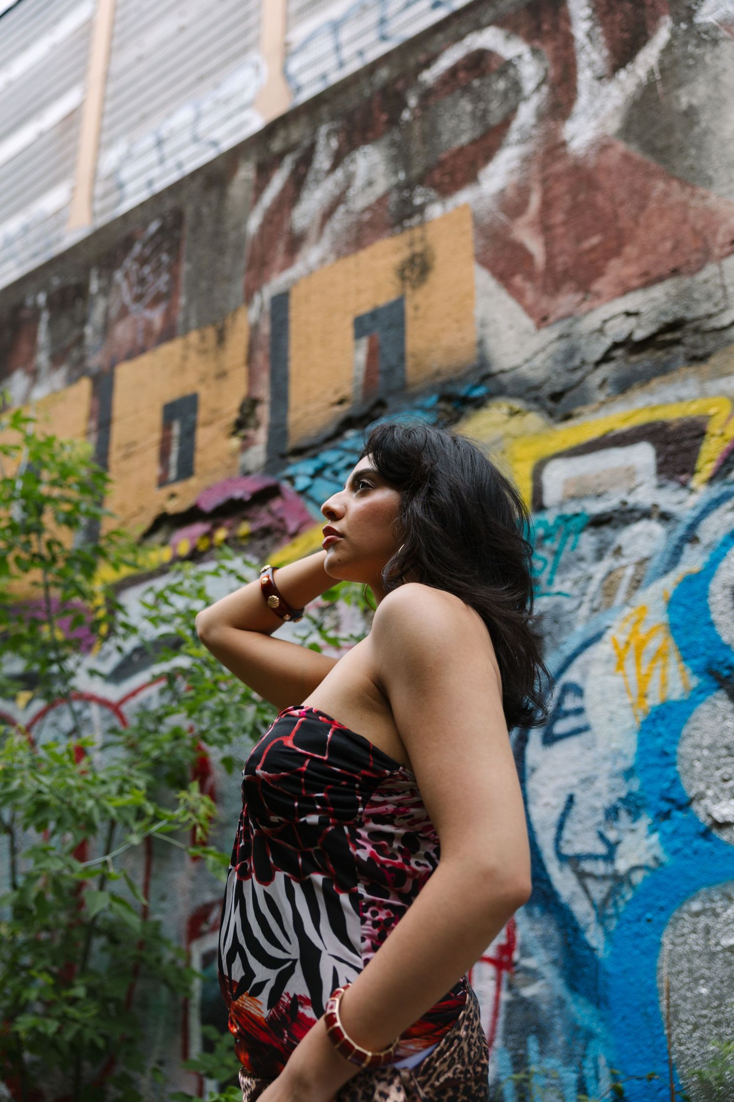 A young woman in a strapless floral dress poses confidently in front of a colorful graffiti-covered urban wall.