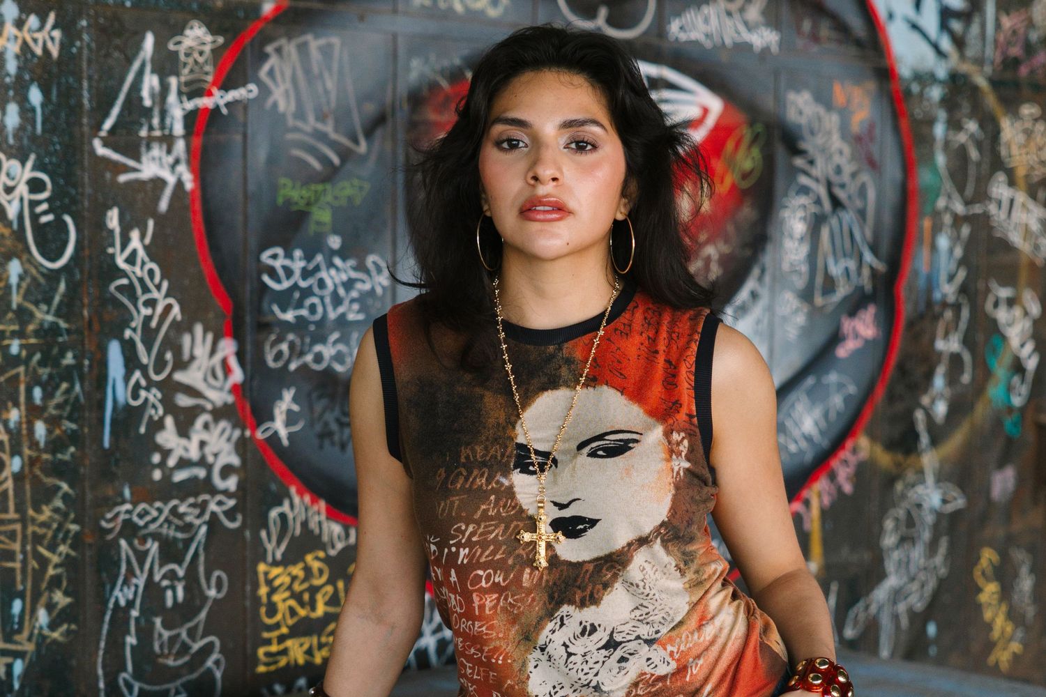 Young woman in graphic tee poses confidently before a colorful graffiti wall with a bold red circle.