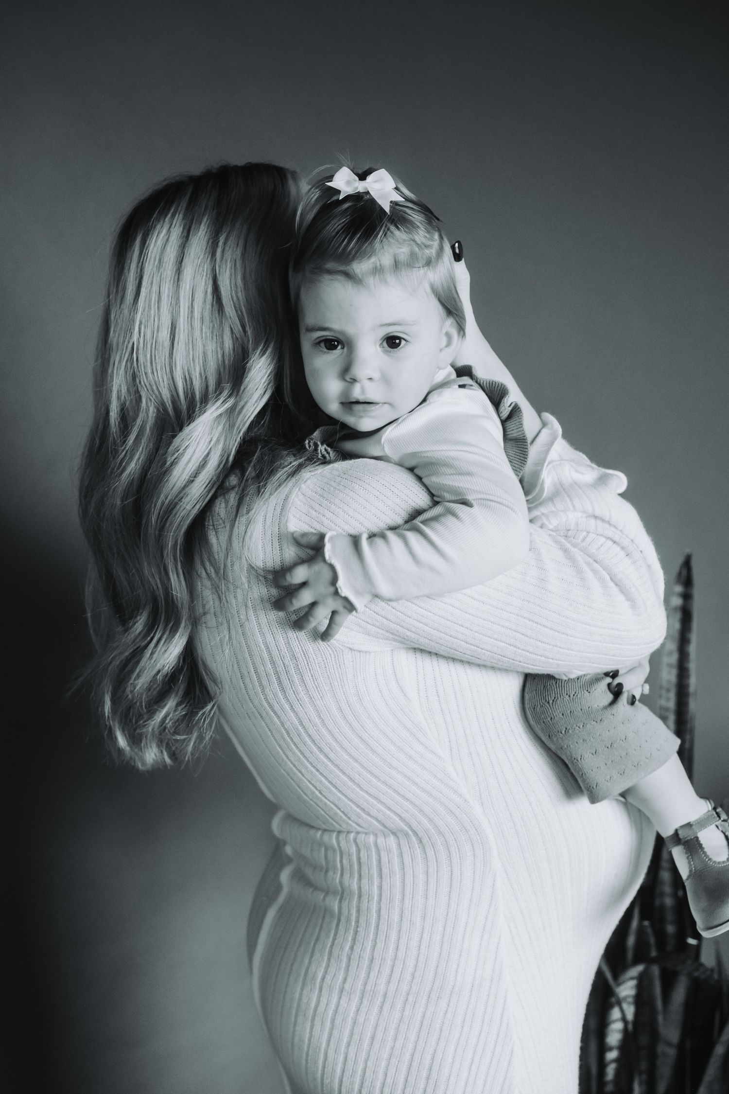Black and white portrait of parent holding small child in white knit sweater.