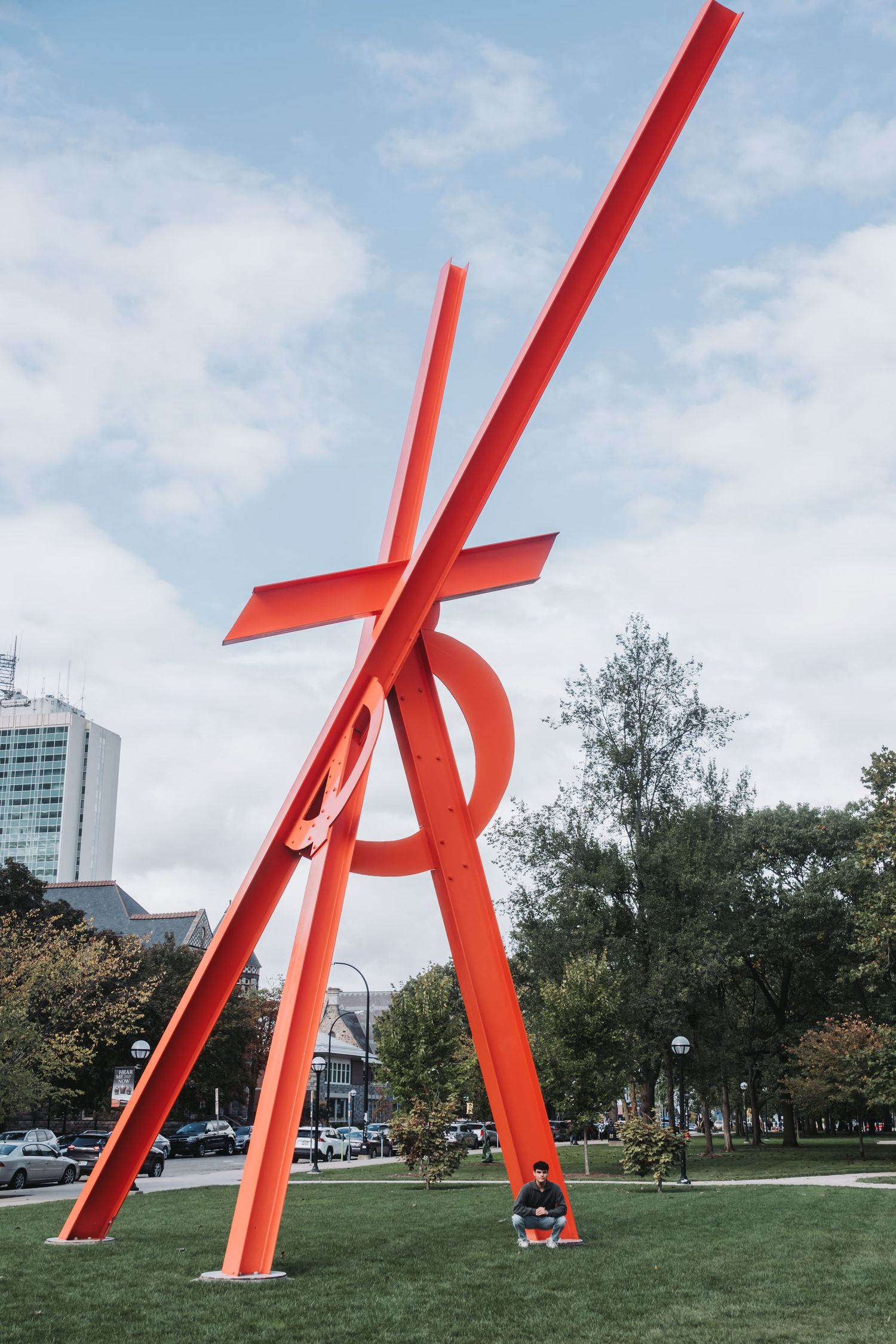 Large red angular metal sculpture installation in an urban park setting.